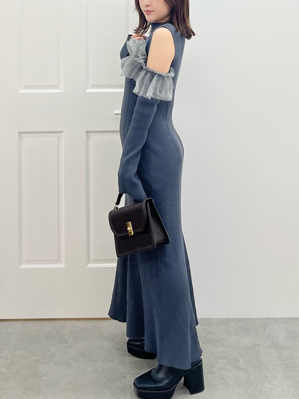 グレー系のワンピース、ブラウン系のハンドバッグ、ブラック系のブーツを着用したレディースの秋コーディネートの7枚目の写真