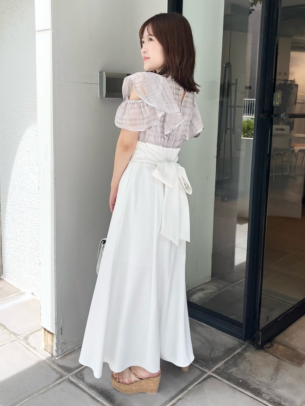 パープル系のワンピース、ブラウン系のサンダル、シルバー系のハンドバッグを着用したレディースの夏コーディネートの2枚目の写真