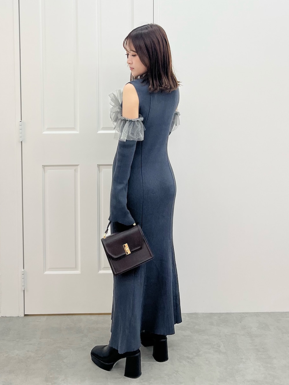 グレー系のワンピース、ブラウン系のハンドバッグ、ブラック系のブーツを着用したレディースの秋コーディネートの3枚目の写真