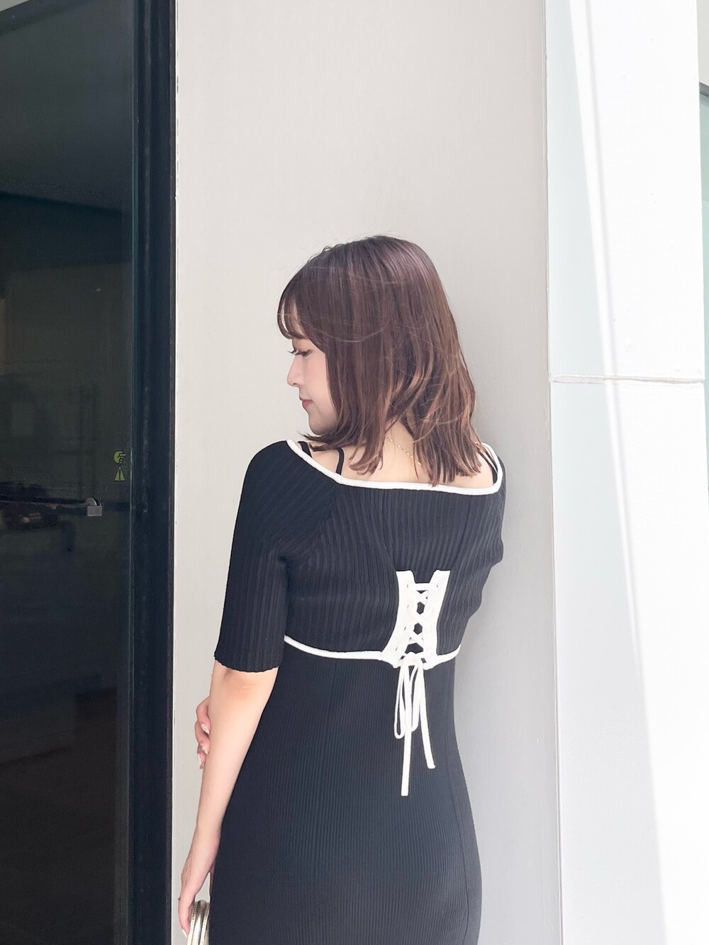 ブラック系のワンピース、ゴールド系のハンドバッグ、ホワイト系のブーツを着用したレディースの夏コーディネートの6枚目の写真