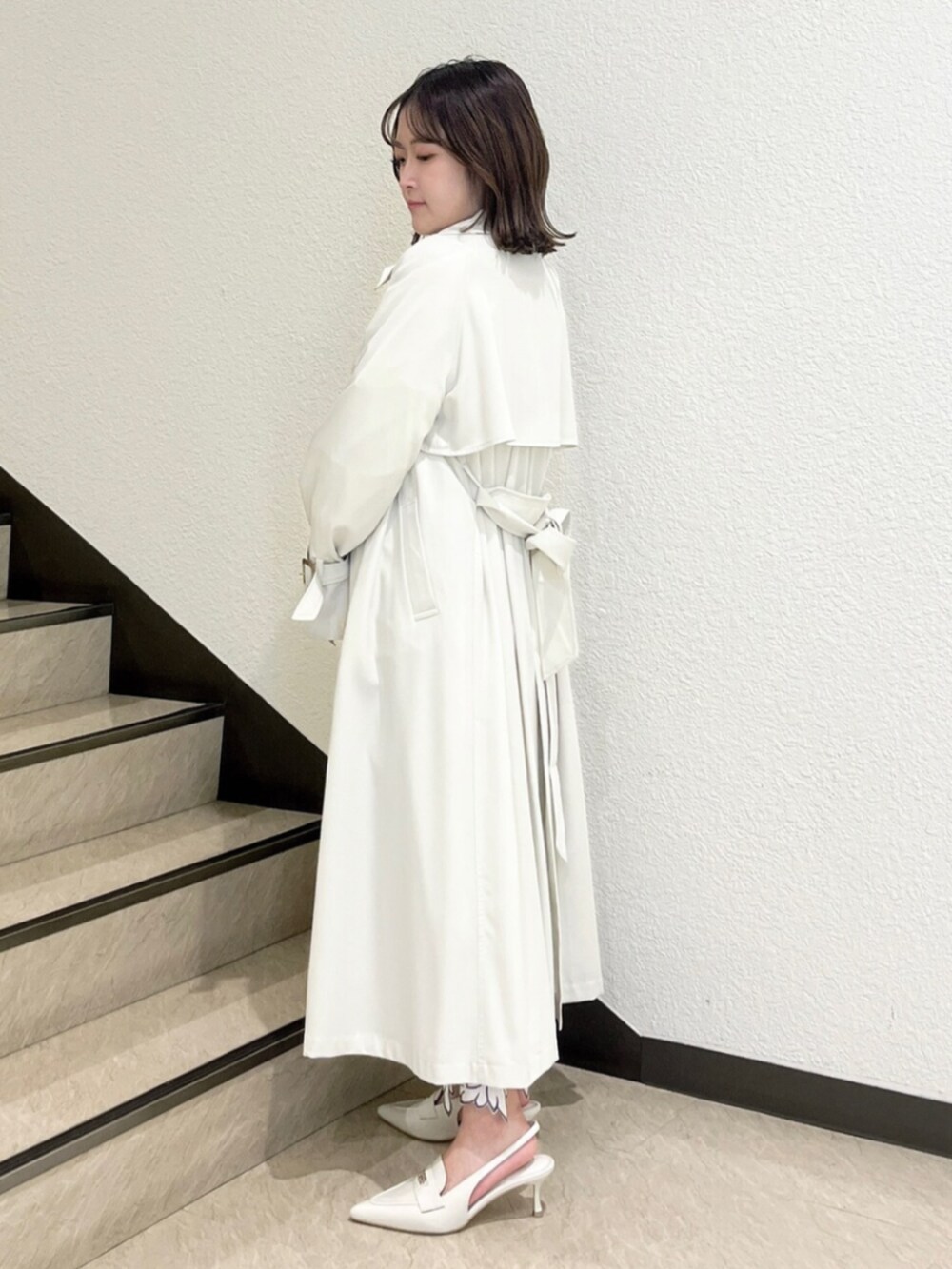 イエロー系のトレンチコート、ホワイト系のニット/セーター、ホワイト系のスカートを着用したレディースの冬コーディネートの2枚目の写真