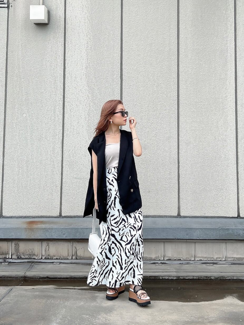 その他のサンダル、ブラック系のベスト、ホワイト系のハンドバッグを着用したレディースの夏コーディネートの2枚目の写真