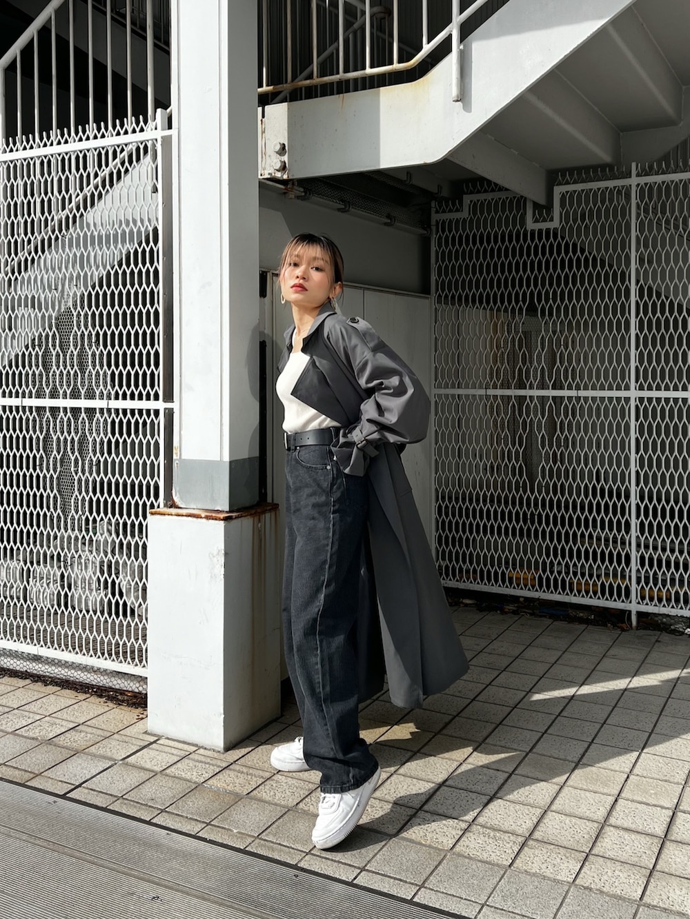 グレー系のトレンチコート、ブラック系のデニムパンツ、ブラック系のベルトを着用したレディースの冬コーディネートの3枚目の写真