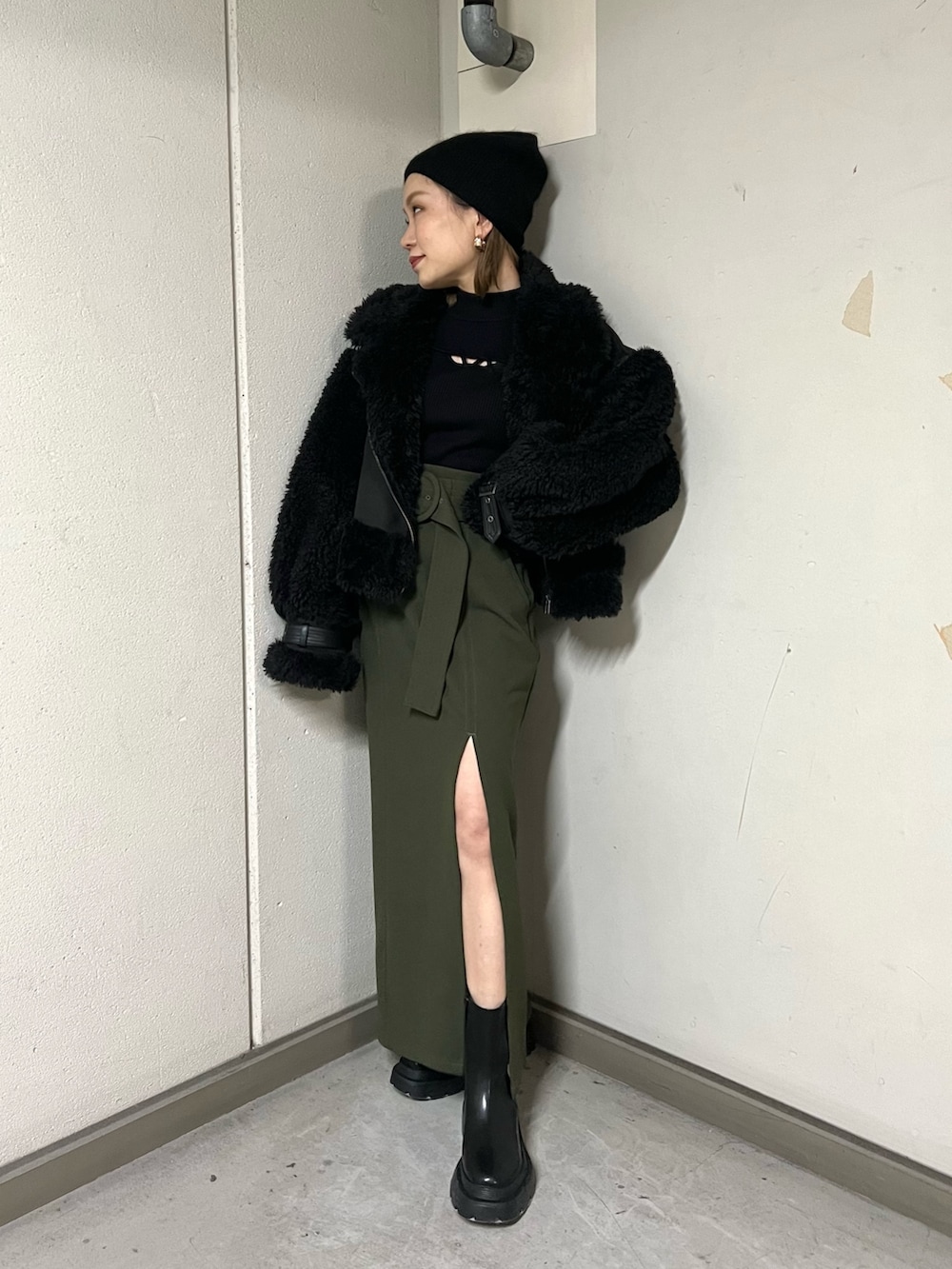 ブラック系のムートンコート、ブラック系のニット/セーター、グリーン系のスカートを着用したレディースの冬コーディネートの2枚目の写真