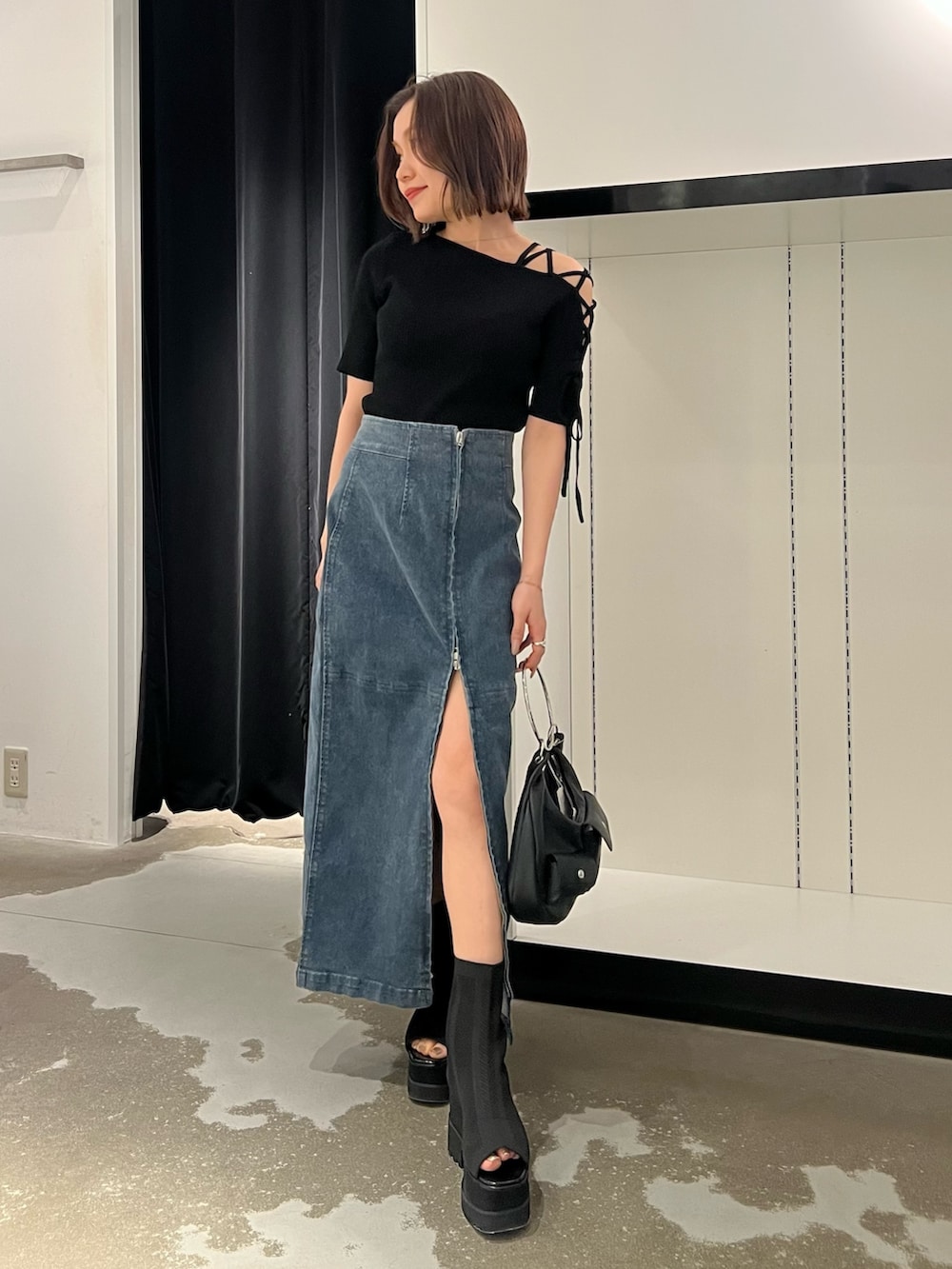 ブルー系のデニムスカート、ブラック系のニット/セーター、ブラック系のサンダルを着用したレディースの夏コーディネートの3枚目の写真