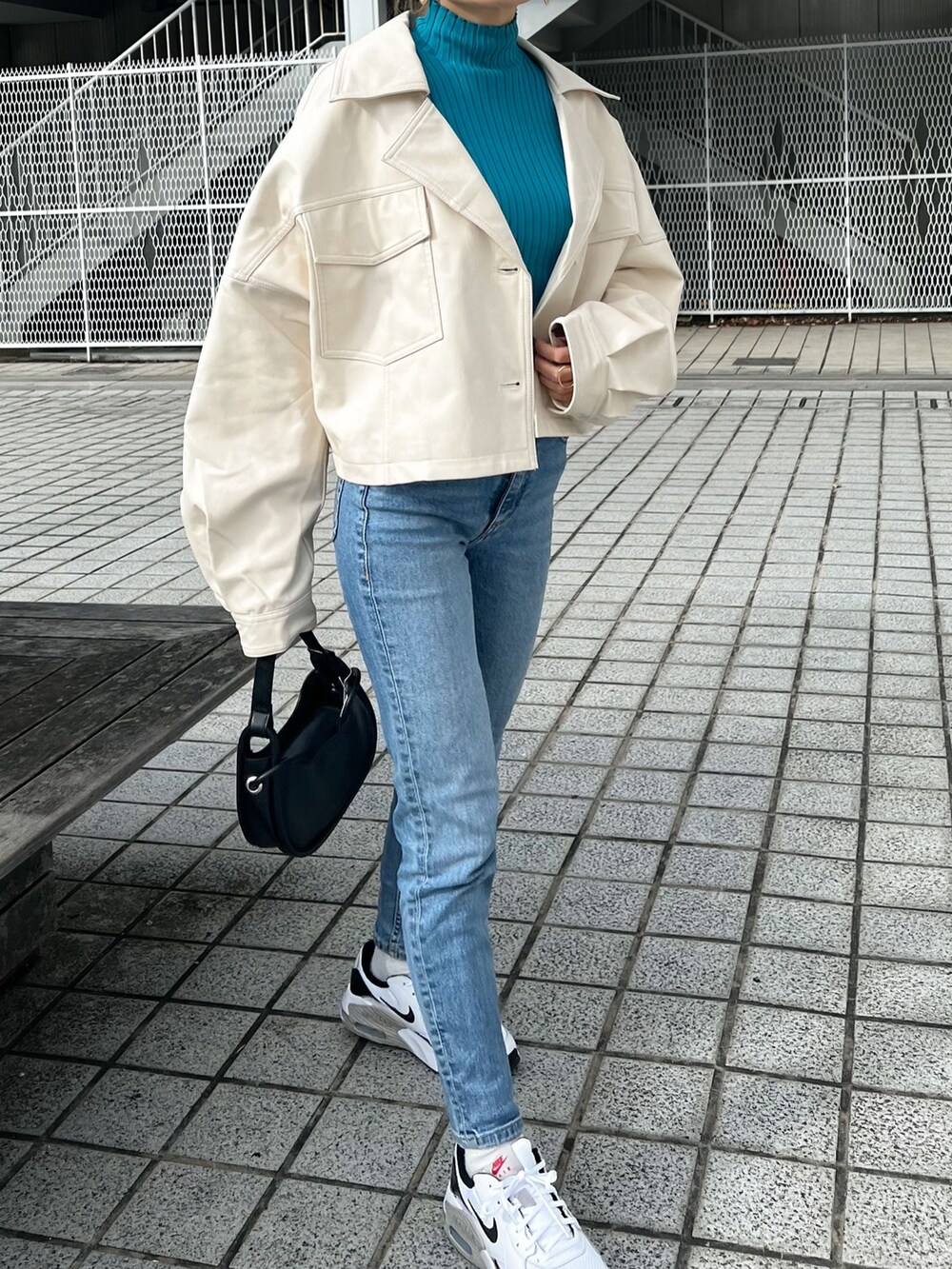 ホワイト系のライダースジャケット、ブルー系のニット/セーター、ブラック系のハンドバッグを着用したレディースの冬コーディネートの5枚目の写真