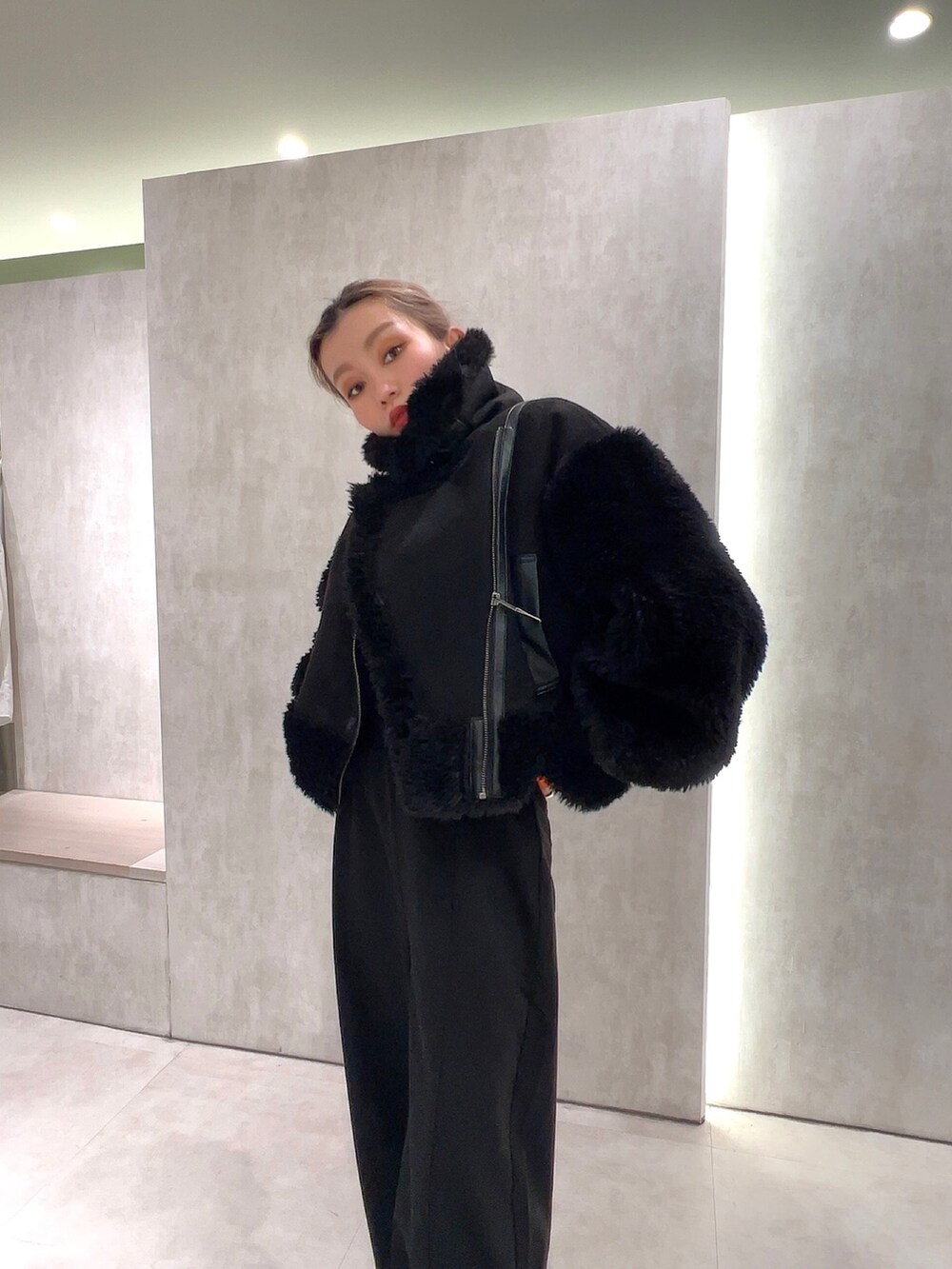 ブラック系のスラックス、オレンジ系のニット/セーター、ブラック系のムートンコートを着用したレディースの冬コーディネートの5枚目の写真