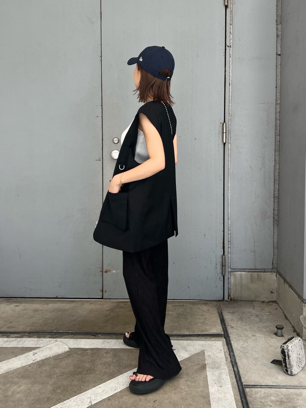 ブラック系のベスト、ホワイト系のニット/セーター、ブルー系のキャップを着用したレディースの夏コーディネートの2枚目の写真