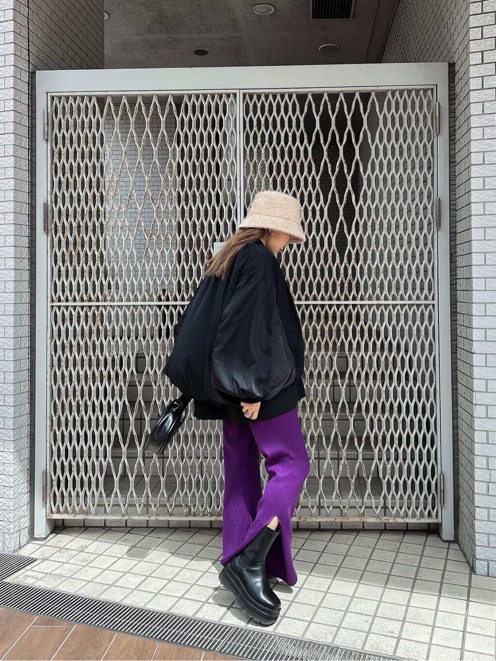 ブラック系のハンドバッグ、ブラック系のニット/セーター、パープル系のスラックスを着用したレディースの秋コーディネートの3枚目の写真