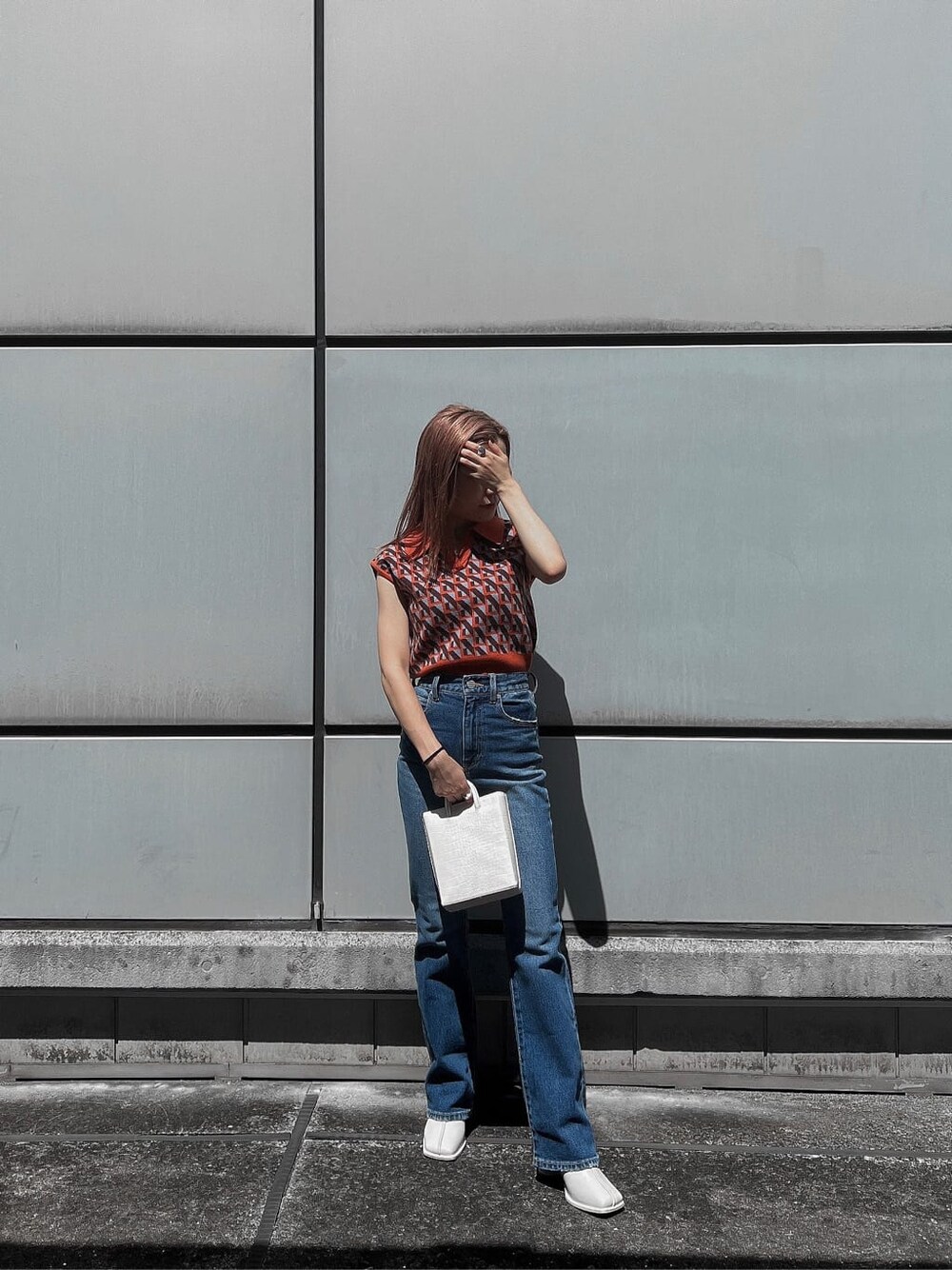 ブルー系のデニムパンツ、オレンジ系のニット/セーター、ホワイト系のブーツを着用したレディースの夏コーディネートの4枚目の写真