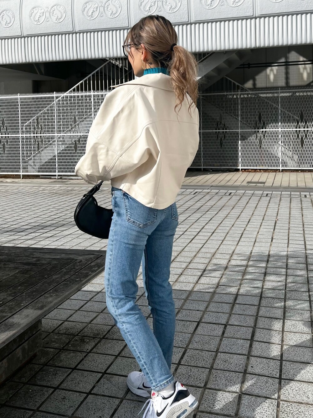 ホワイト系のライダースジャケット、ブルー系のニット/セーター、ブラック系のハンドバッグを着用したレディースの冬コーディネートの6枚目の写真