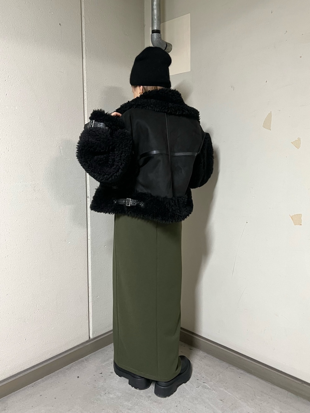 ブラック系のムートンコート、ブラック系のニット/セーター、グリーン系のスカートを着用したレディースの冬コーディネートの3枚目の写真