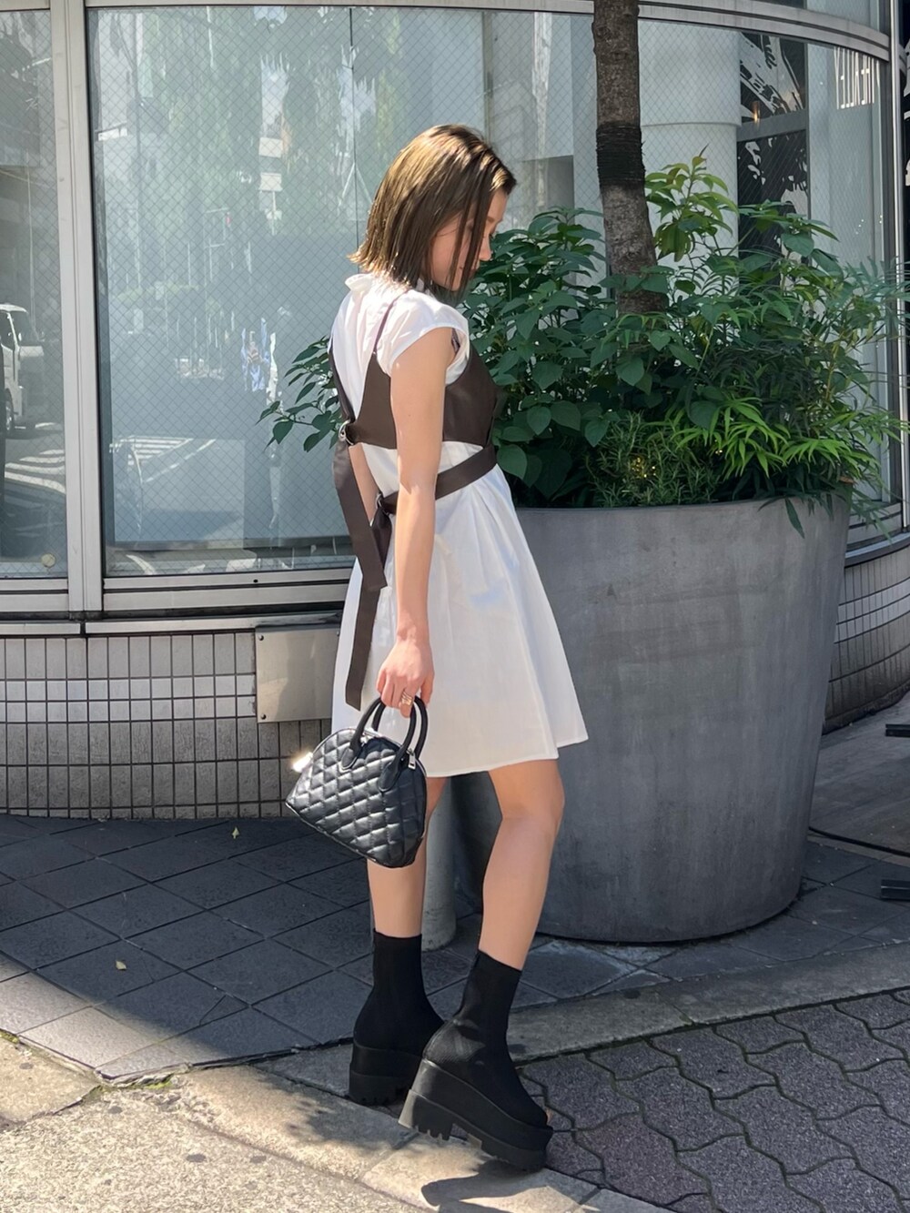 ブラウン系のワンピース、ブラック系のハンドバッグ、ブラック系のブーツを着用したレディースの春コーディネートの3枚目の写真