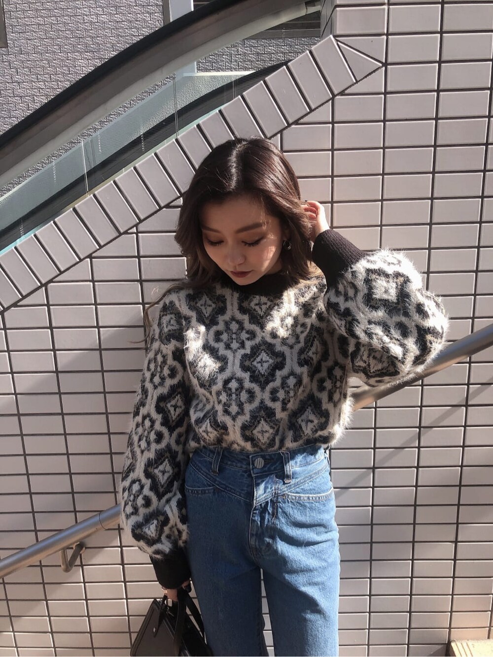 ブルー系のデニムパンツ、ブラック系のハンドバッグ、ブラック系のニット/セーターを着用したレディースの秋コーディネートの2枚目の写真