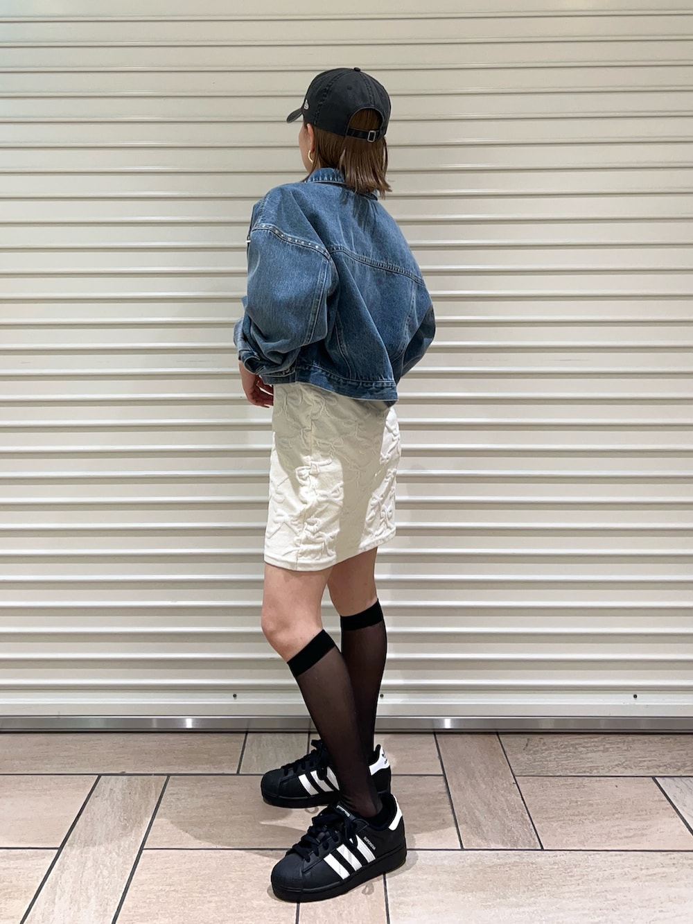 ブルー系のデニムジャケット、ホワイト系のワンピース、ブラック系のキャップを着用したレディースの春コーディネートの2枚目の写真