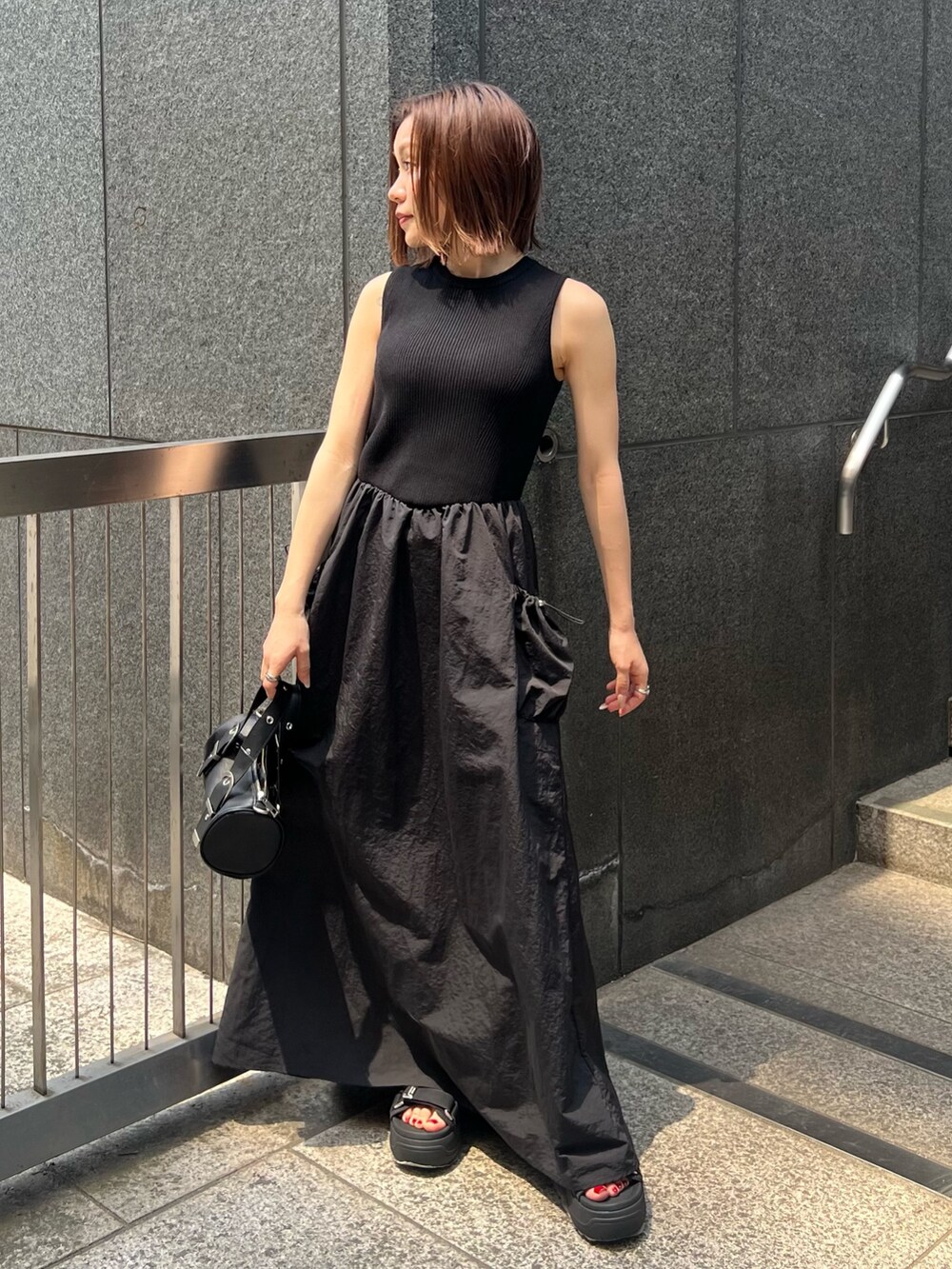 ブラック系のワンピース、ブラック系のサンダル、ブラック系のハンドバッグを着用したレディースの夏コーディネートの2枚目の写真