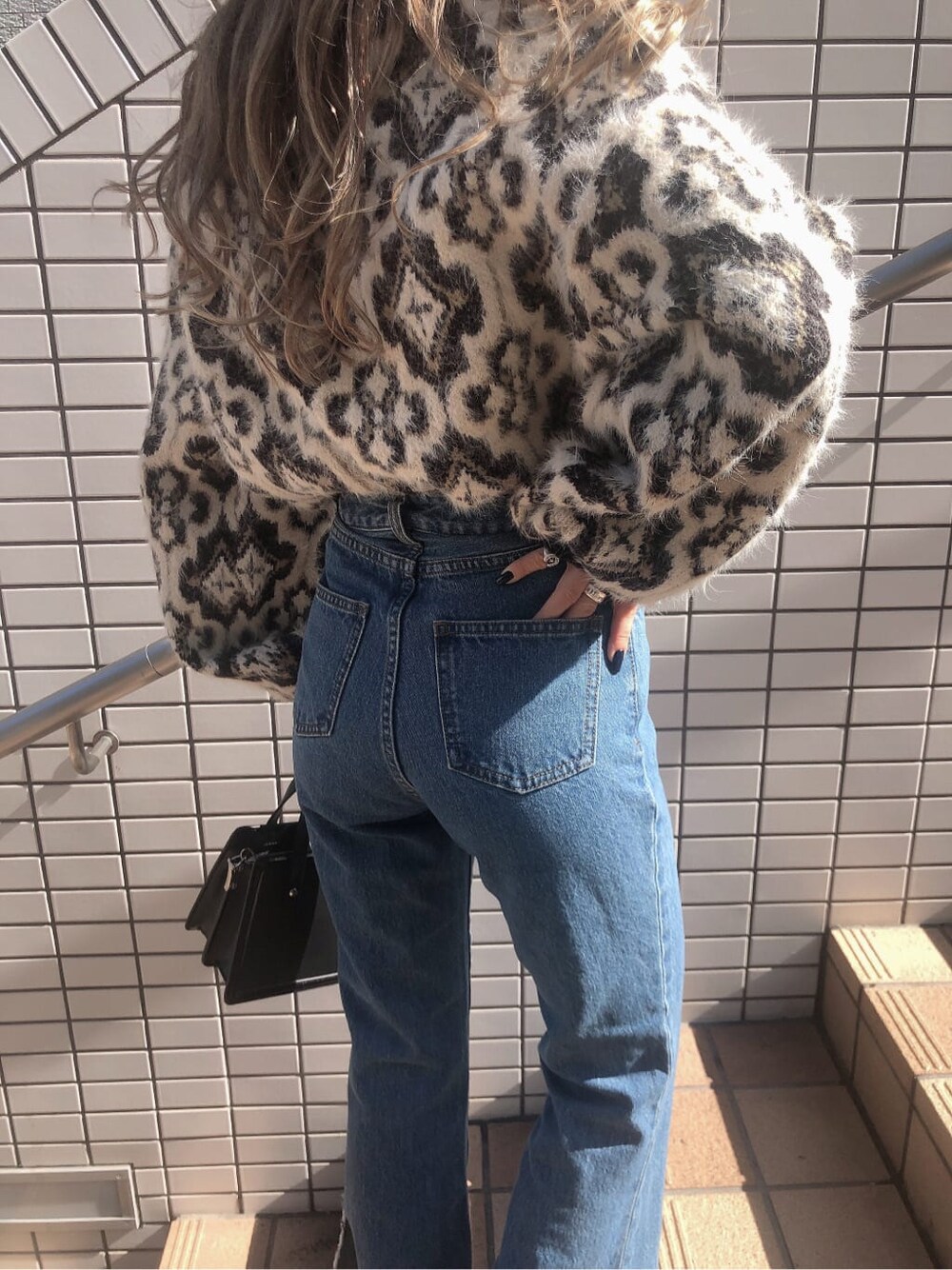 ブルー系のデニムパンツ、ブラック系のハンドバッグ、ブラック系のニット/セーターを着用したレディースの秋コーディネートの4枚目の写真