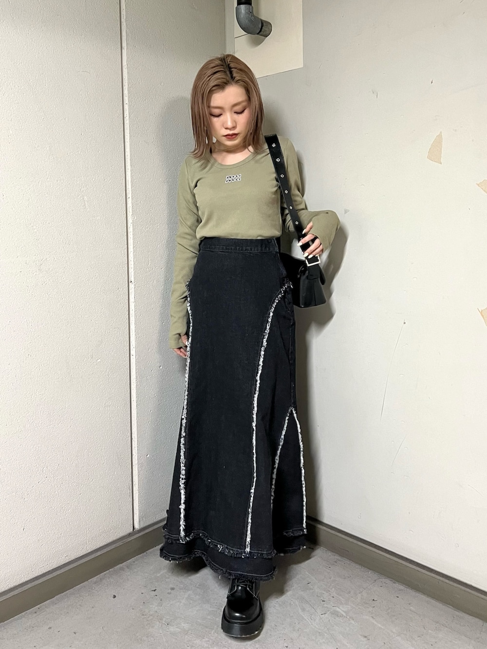 グリーン系のTシャツ/カットソー、ブラック系のデニムスカート、ブラック系のブーツを着用したレディースの冬コーディネートの2枚目の写真