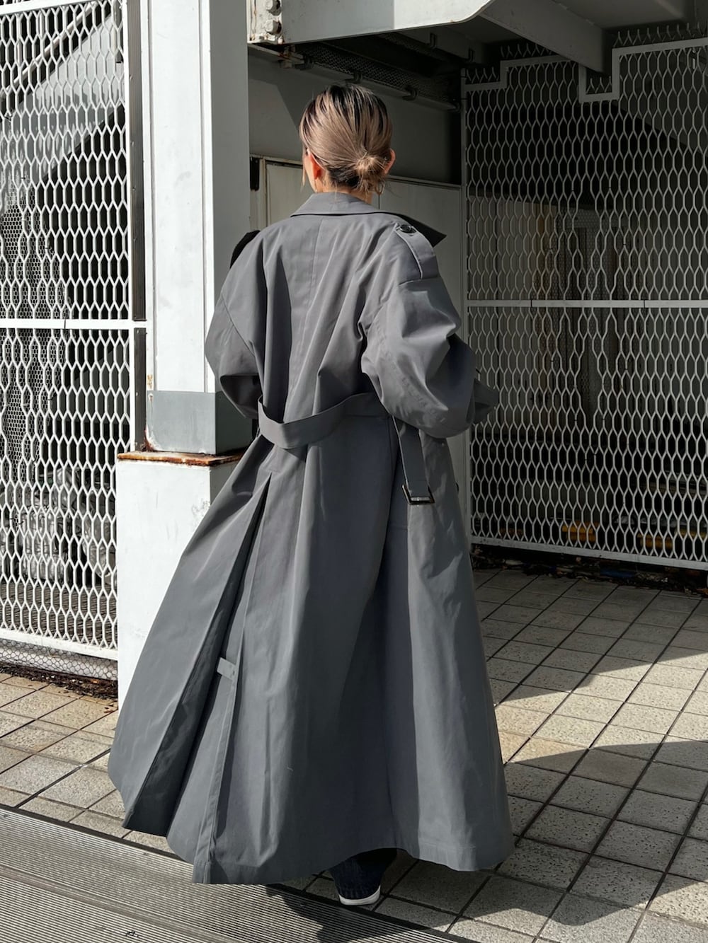 グレー系のトレンチコート、ブラック系のデニムパンツ、ブラック系のベルトを着用したレディースの冬コーディネートの5枚目の写真