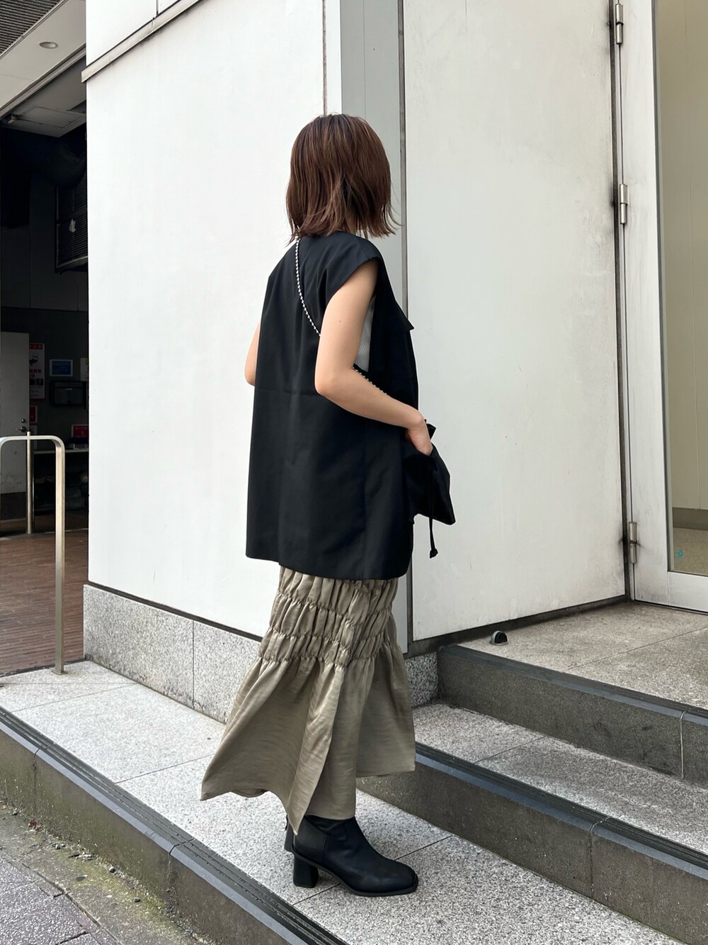 ブラック系のベスト、ホワイト系のニット/セーター、グリーン系のスカートを着用したレディースの夏コーディネートの3枚目の写真