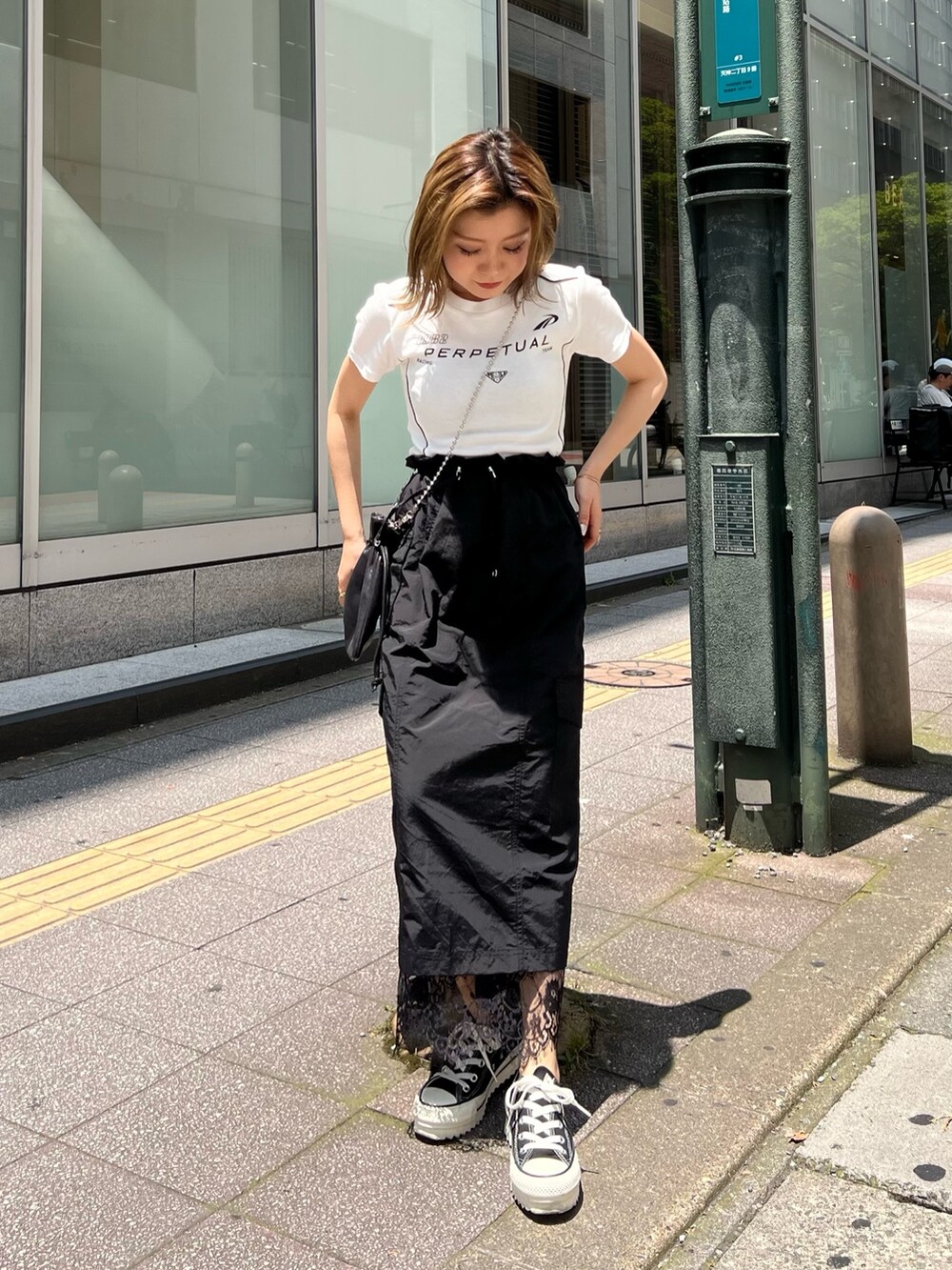 ブラック系のスカート、ブラック系のショルダーバッグ、ホワイト系のTシャツ/カットソーを着用したレディースの夏コーディネートの2枚目の写真