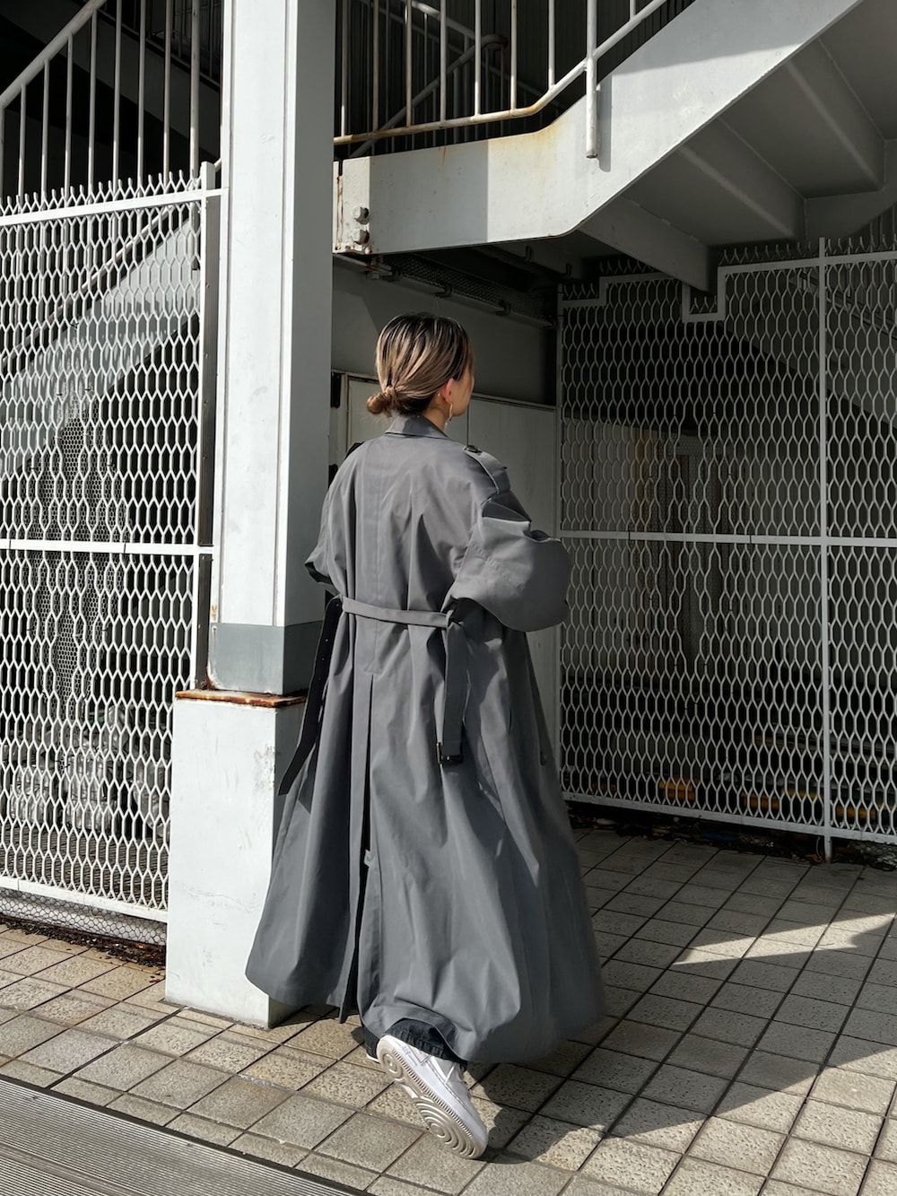 グレー系のトレンチコート、ブラック系のデニムパンツ、ブラック系のベルトを着用したレディースの冬コーディネートの2枚目の写真