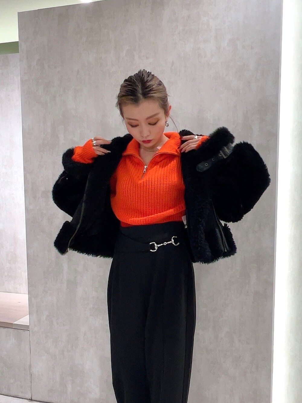 ブラック系のスラックス、オレンジ系のニット/セーター、ブラック系のムートンコートを着用したレディースの冬コーディネートの3枚目の写真