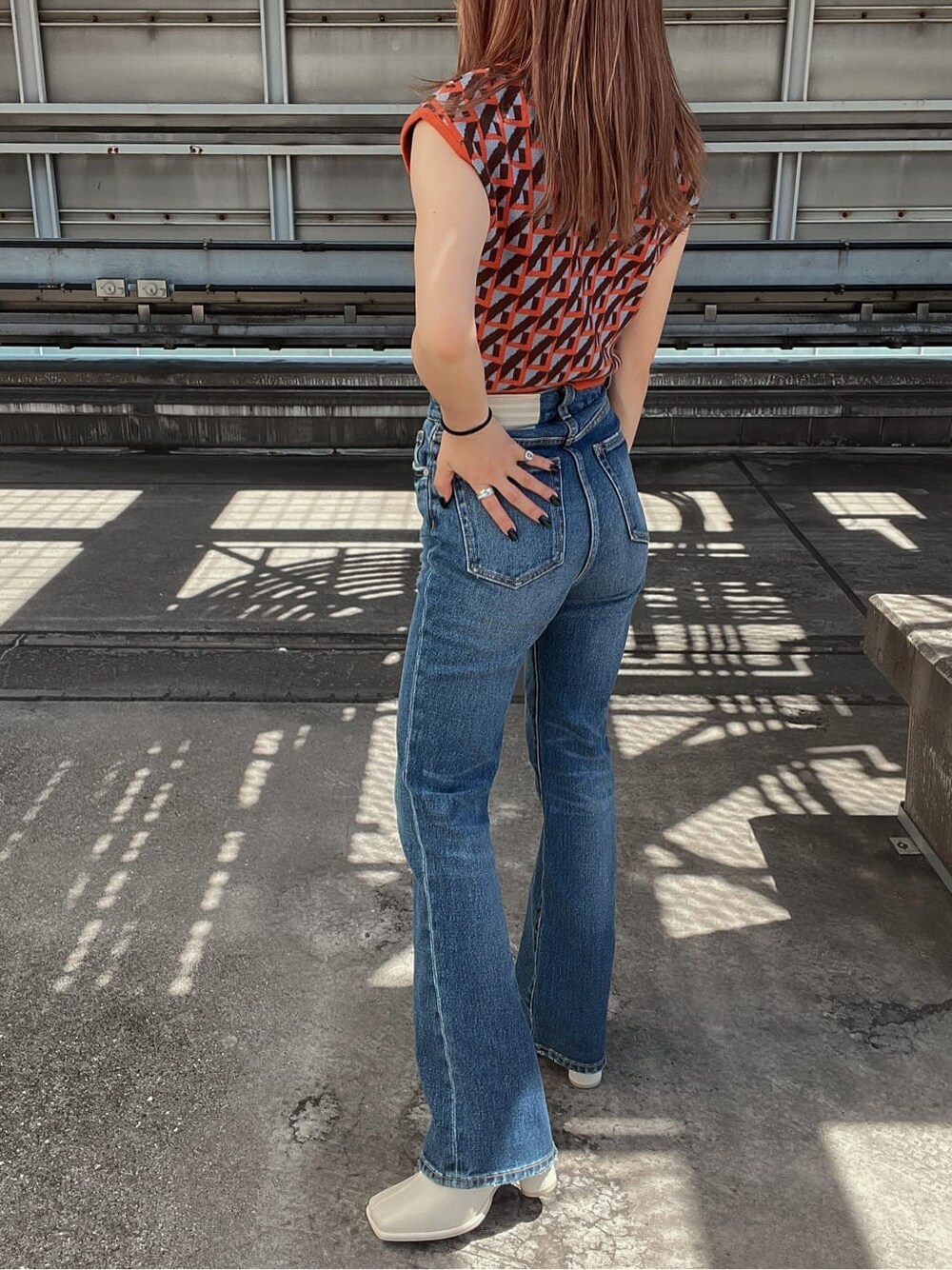 ブルー系のデニムパンツ、オレンジ系のニット/セーター、ホワイト系のブーツを着用したレディースの夏コーディネートの2枚目の写真