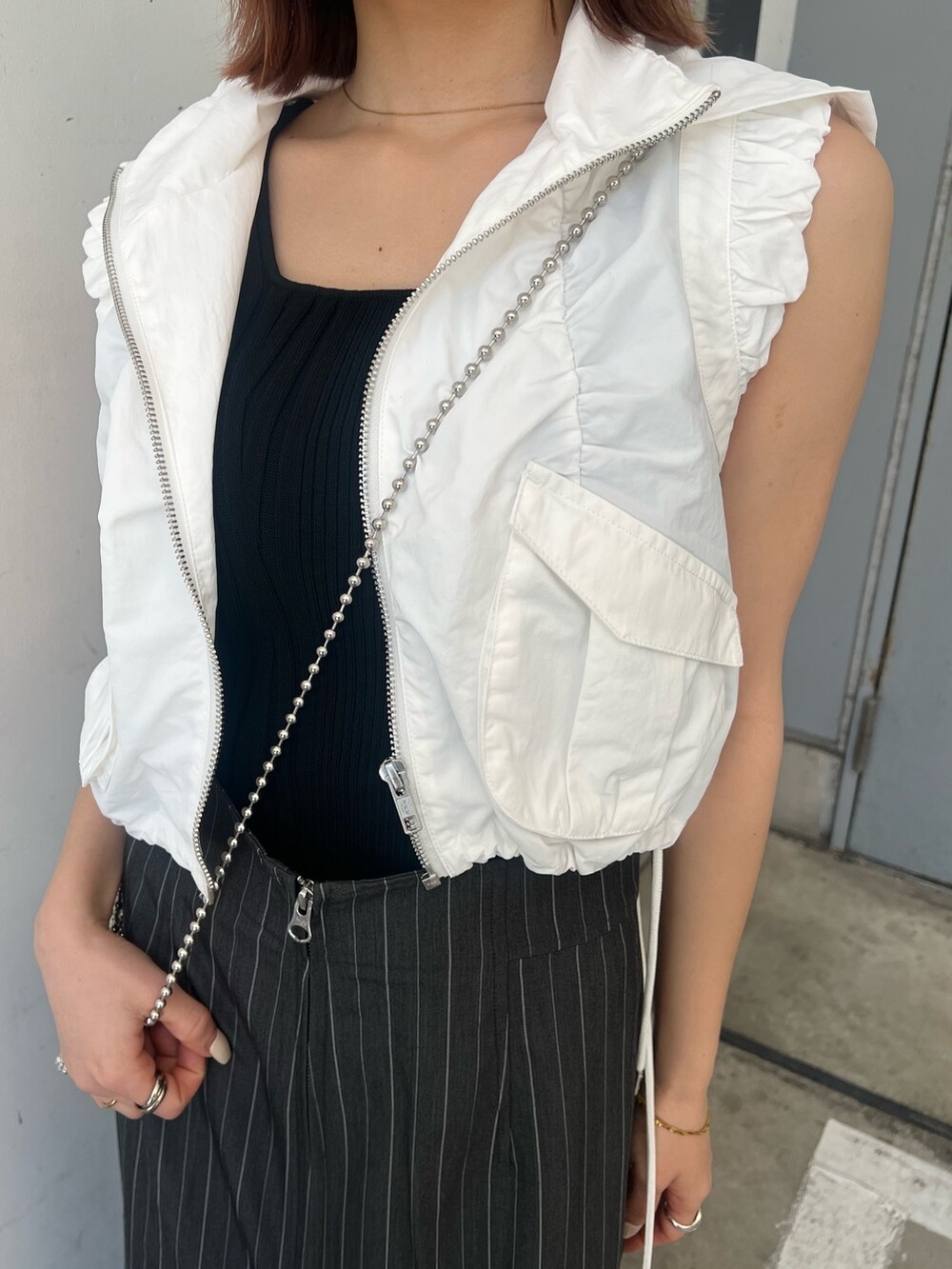 ホワイト系のベスト、ブラック系のタンクトップ、グレー系のスカートを着用したレディースの春コーディネートの7枚目の写真