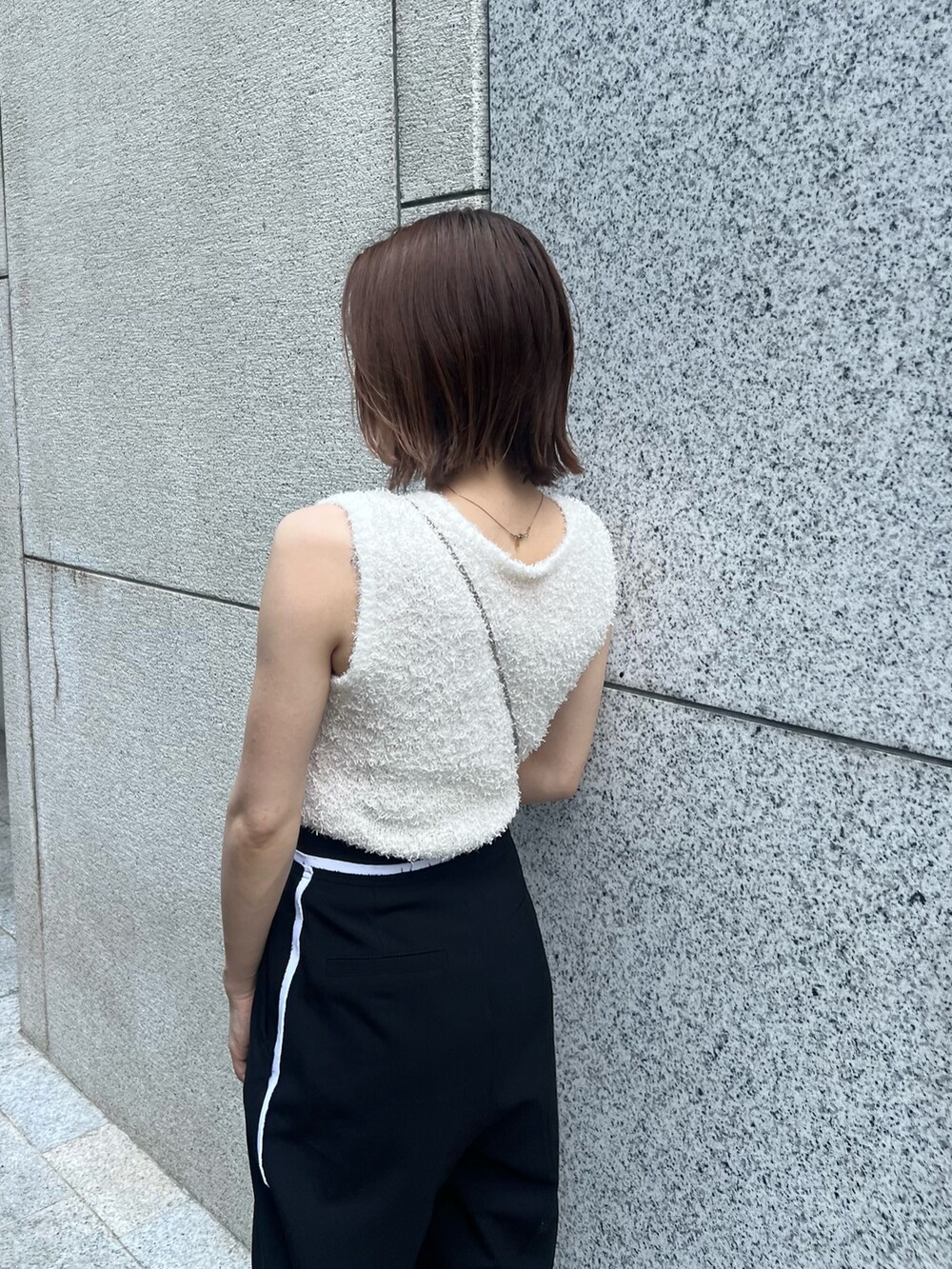 ホワイト系のニット/セーター、ブラック系のその他パンツ、ゴールド系のショルダーバッグを着用したレディースの夏コーディネートの6枚目の写真