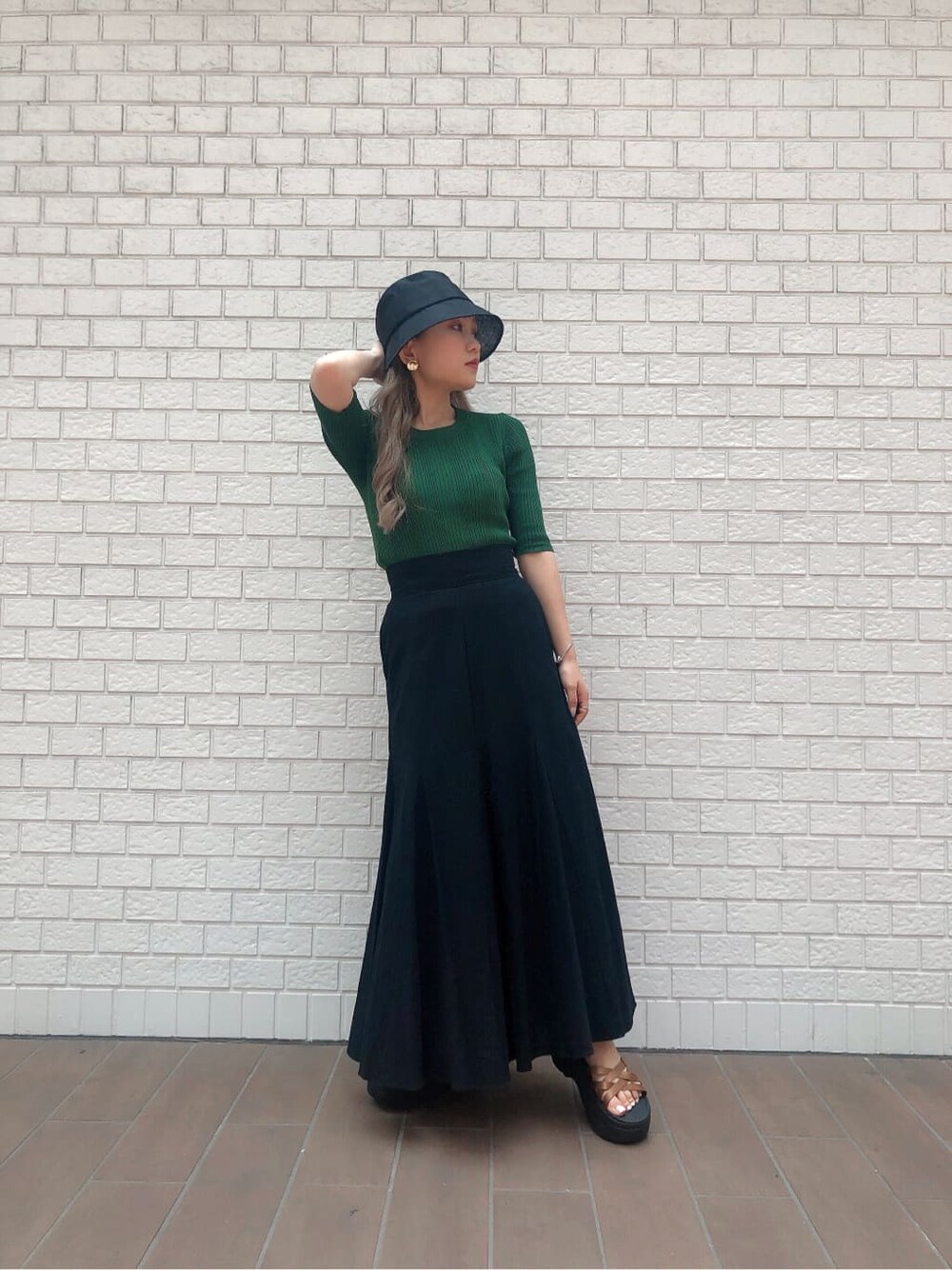 ブラック系のスカート、グリーン系のニット/セーター、ブラック系のハットを着用したレディースの夏コーディネートの2枚目の写真
