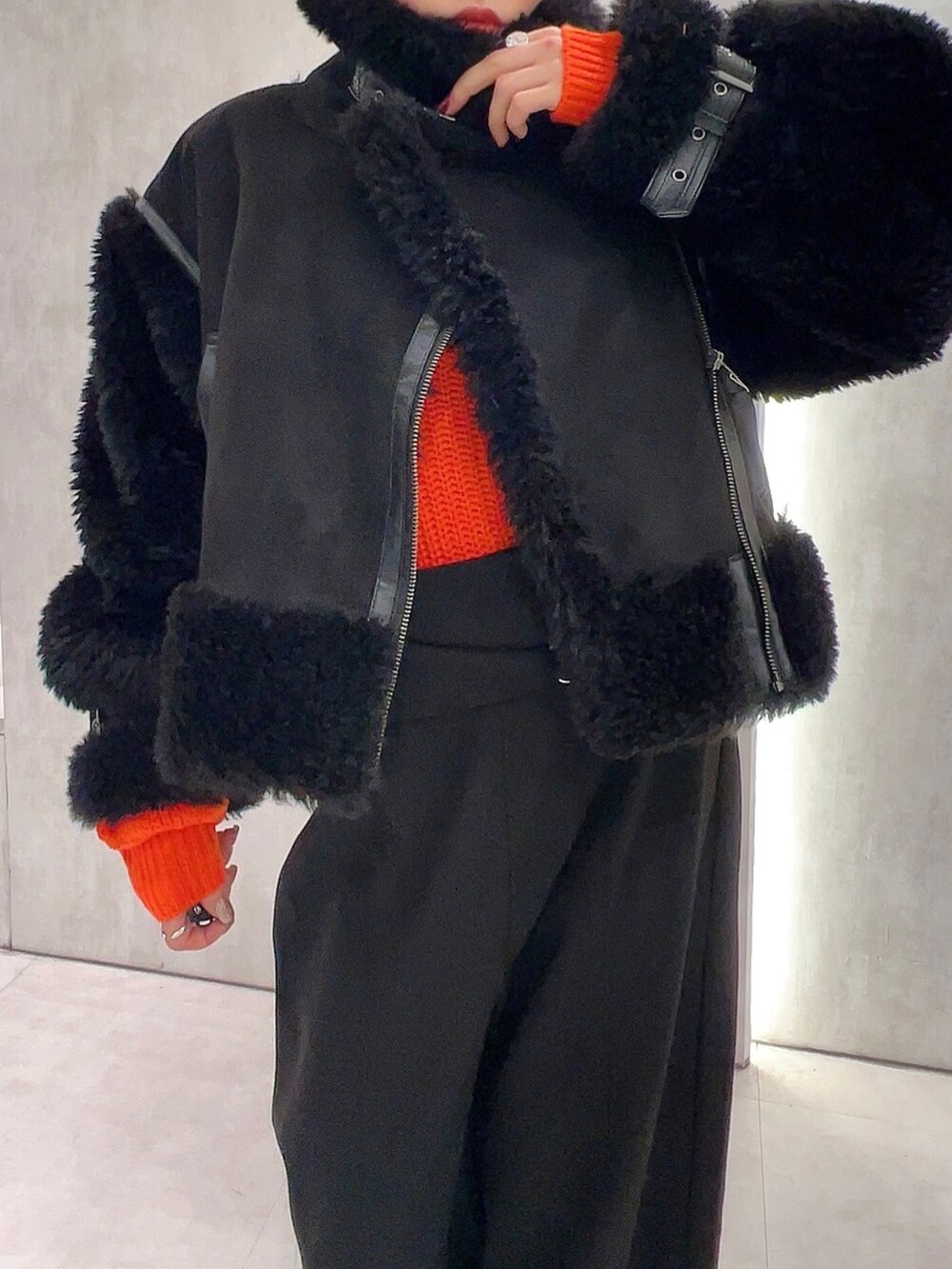 ブラック系のスラックス、オレンジ系のニット/セーター、ブラック系のムートンコートを着用したレディースの冬コーディネートの6枚目の写真