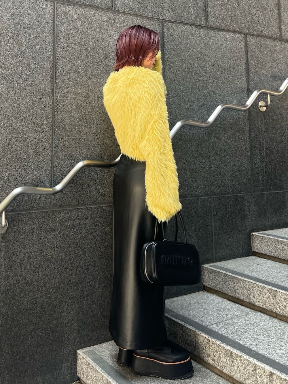 イエロー系のニット/セーター、ブラック系のスカート、ブラック系のブーツを着用したレディースの秋コーディネートの2枚目の写真