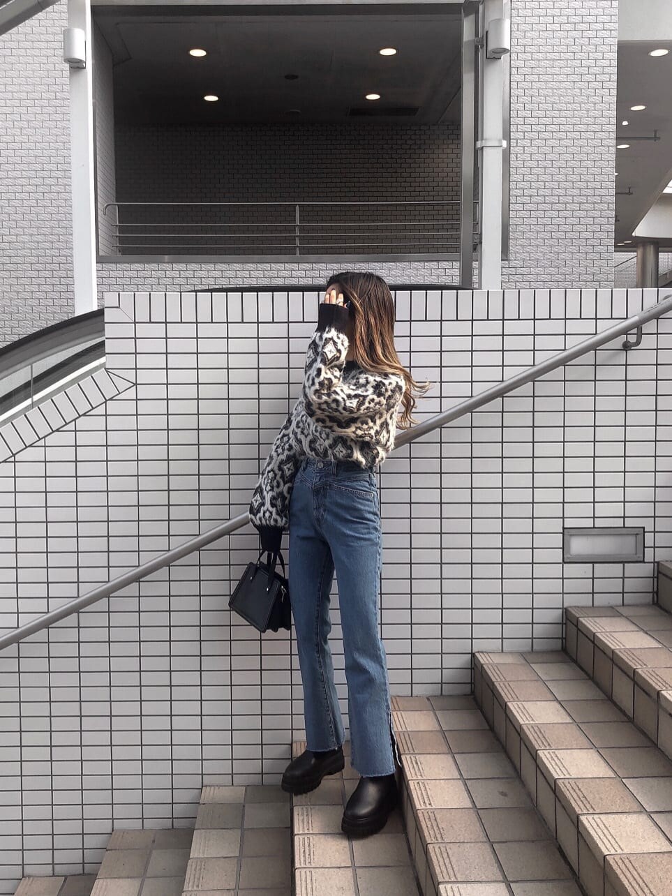 ブルー系のデニムパンツ、ブラック系のハンドバッグ、ブラック系のニット/セーターを着用したレディースの秋コーディネートの3枚目の写真
