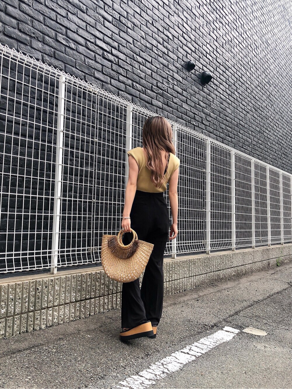 ブラック系のスラックス、ベージュ系のかごバッグ、ブラック系のサンダルを着用したレディースの夏コーディネートの2枚目の写真