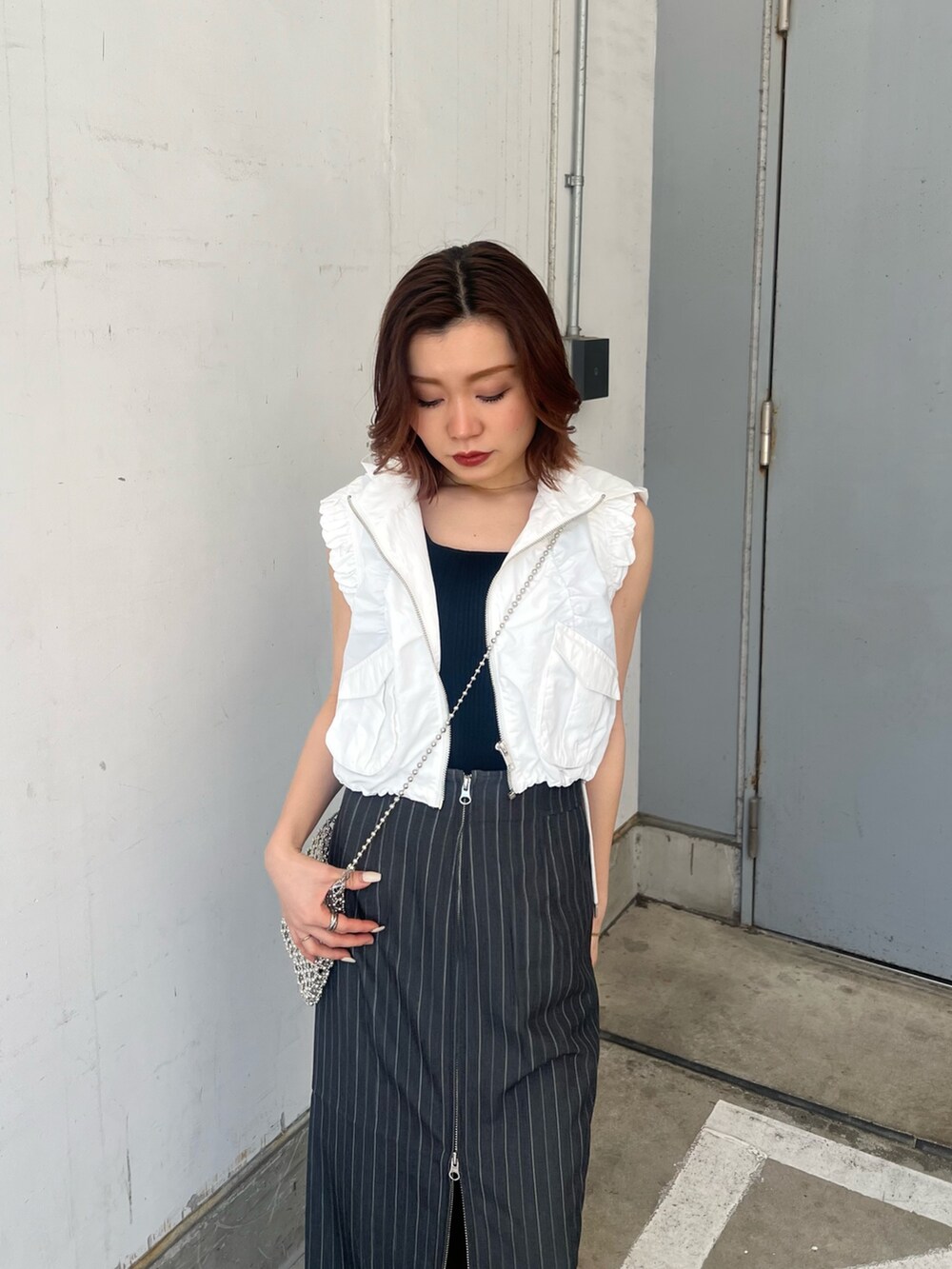 ホワイト系のベスト、ブラック系のタンクトップ、グレー系のスカートを着用したレディースの春コーディネートの6枚目の写真