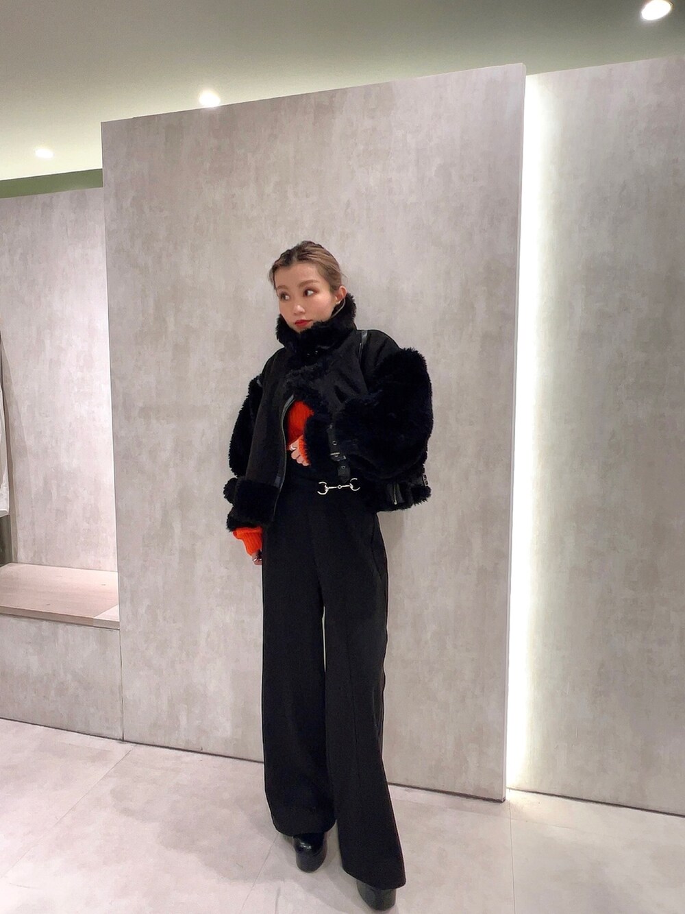 ブラック系のスラックス、オレンジ系のニット/セーター、ブラック系のムートンコートを着用したレディースの冬コーディネートの4枚目の写真