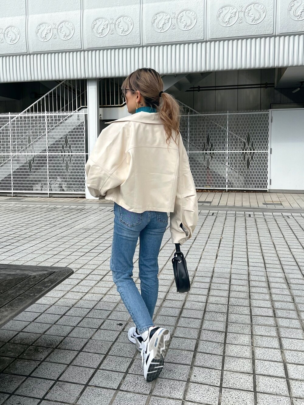 ホワイト系のライダースジャケット、ブルー系のニット/セーター、ブラック系のハンドバッグを着用したレディースの冬コーディネートの3枚目の写真