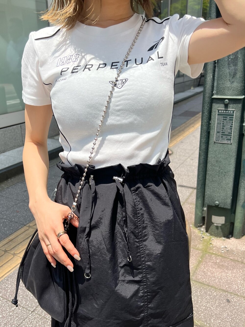 ブラック系のスカート、ブラック系のショルダーバッグ、ホワイト系のTシャツ/カットソーを着用したレディースの夏コーディネートの7枚目の写真