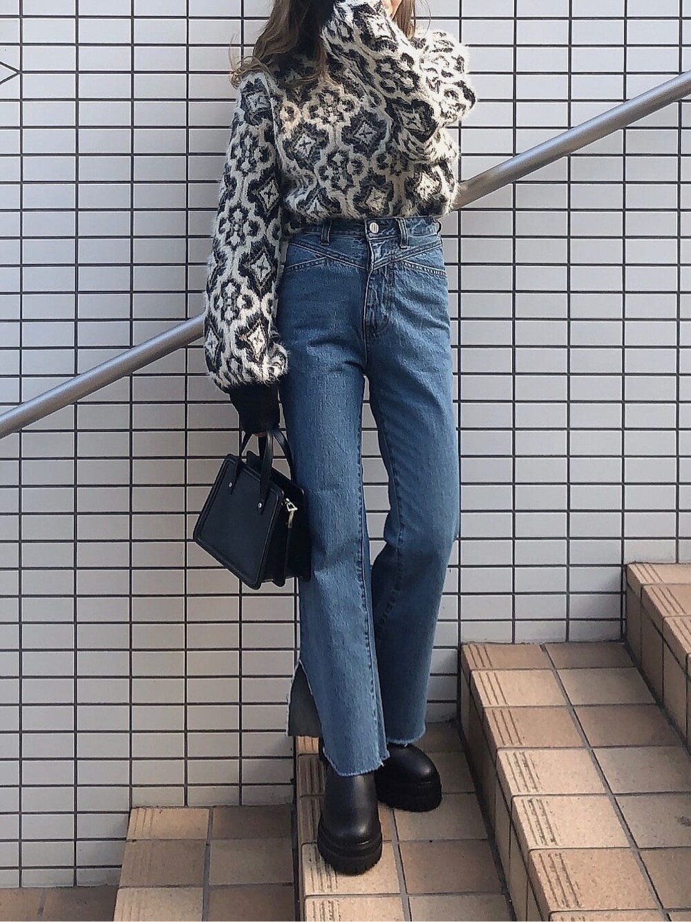 ブルー系のデニムパンツ、ブラック系のハンドバッグ、ブラック系のニット/セーターを着用したレディースの秋コーディネートの5枚目の写真