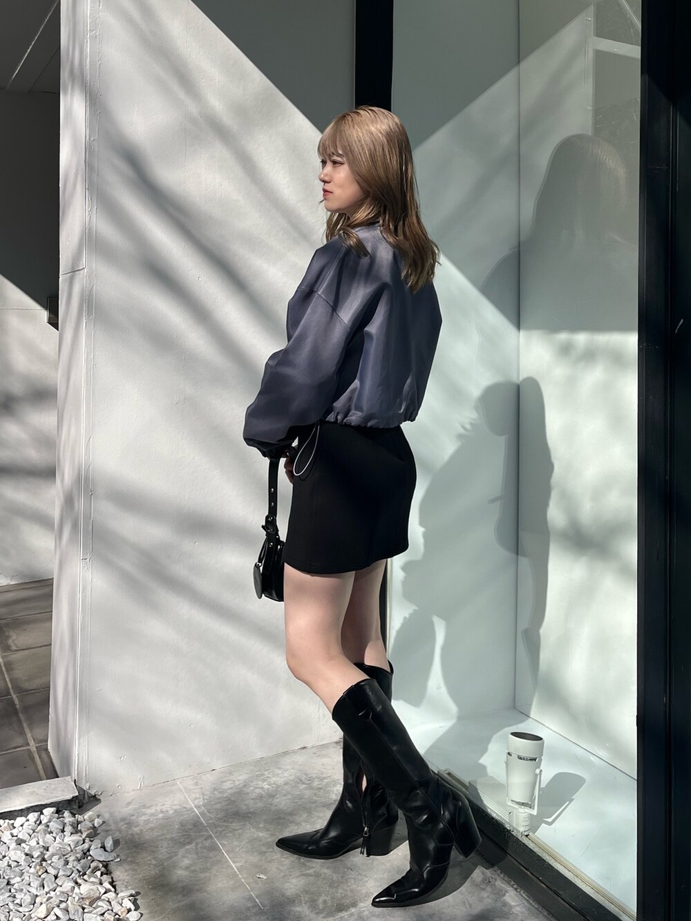 ブラック系のスカート、ブラック系のブーツ、ブラック系のハンドバッグを着用したレディースの冬コーディネートの2枚目の写真