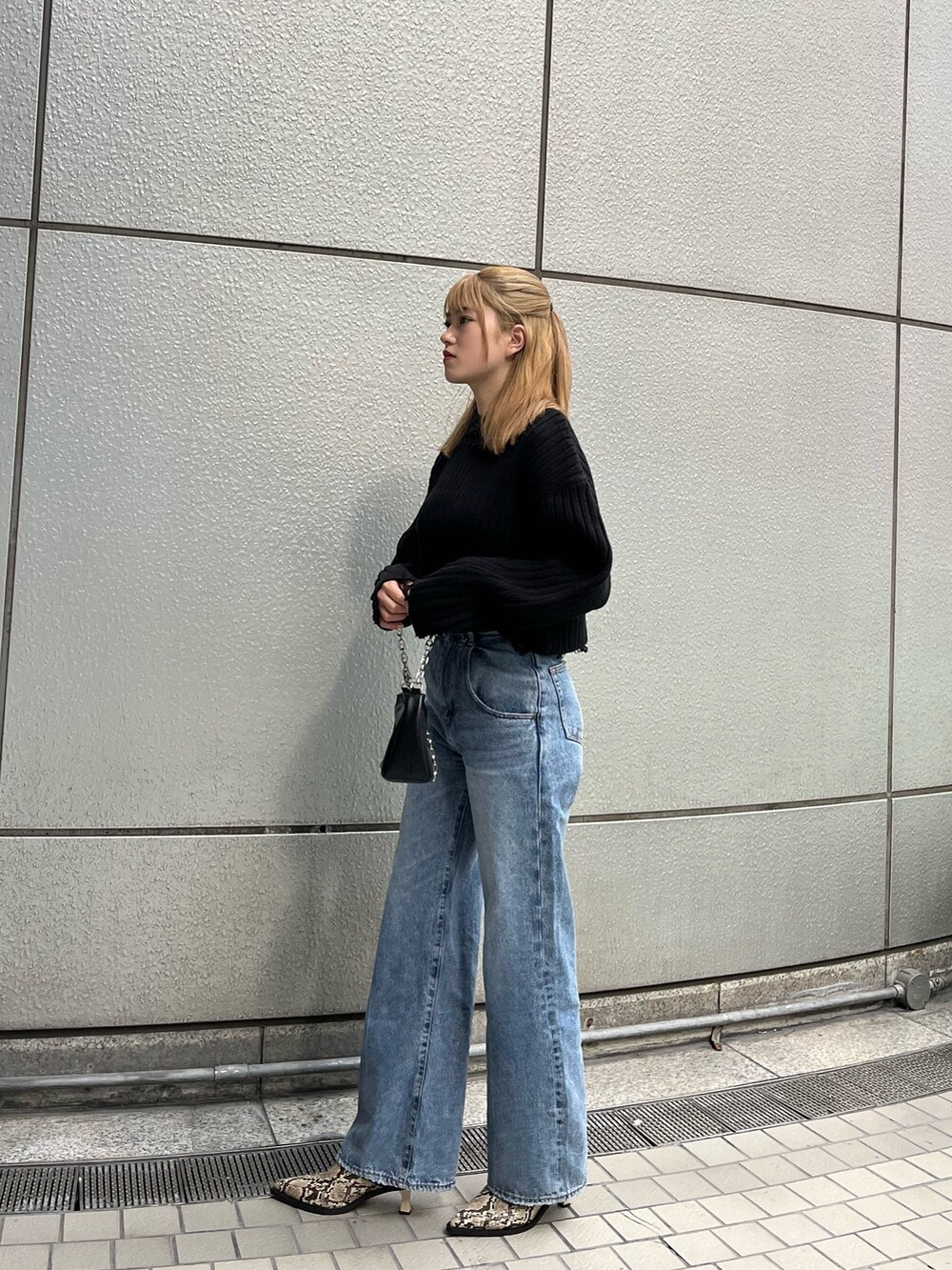 ブルー系のデニムパンツ、ブラック系のニット/セーター、ブラック系のハンドバッグを着用したレディースの秋コーディネートの3枚目の写真