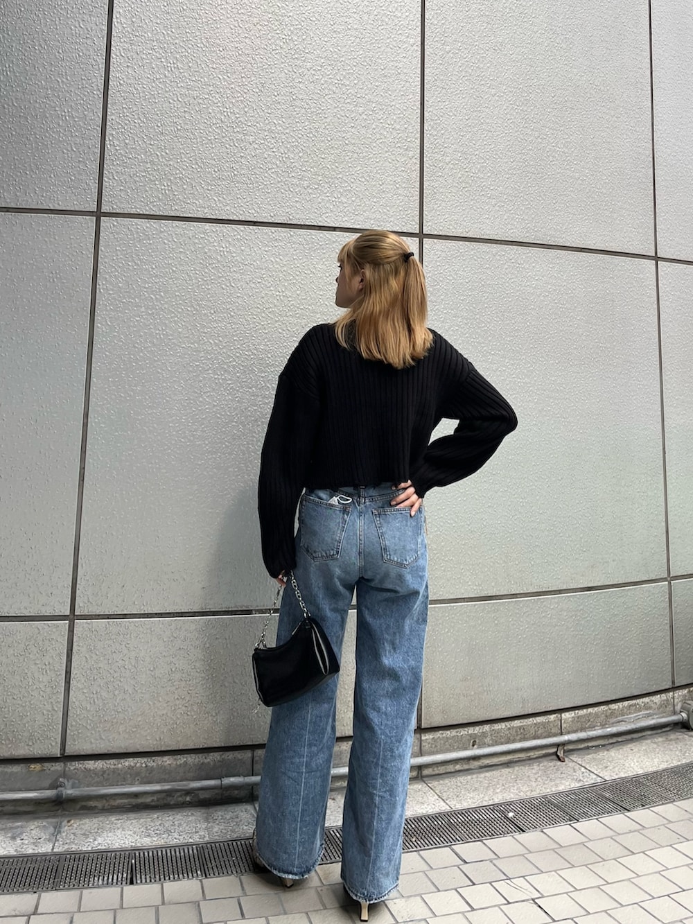 ブルー系のデニムパンツ、ブラック系のニット/セーター、ブラック系のハンドバッグを着用したレディースの秋コーディネートの4枚目の写真