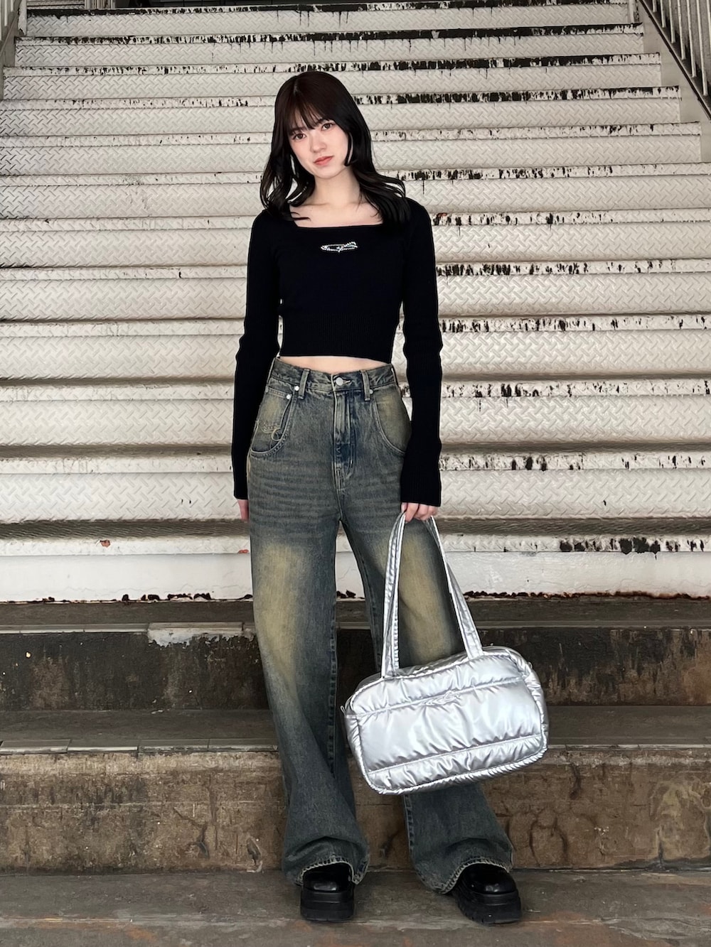 シルバー系のボストンバッグ、ブルー系のデニムパンツ、ブラック系のニット/セーターを着用したレディースの冬コーディネートの2枚目の写真