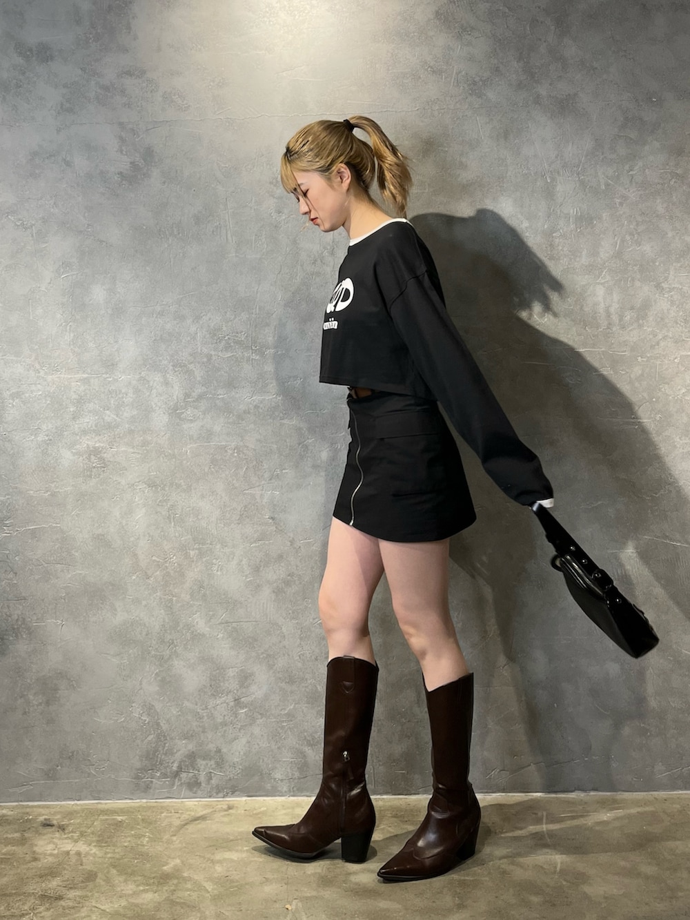 ブラック系のスカート、ブラウン系のブーツ、ブラック系のTシャツ/カットソーを着用したレディースの冬コーディネートの2枚目の写真