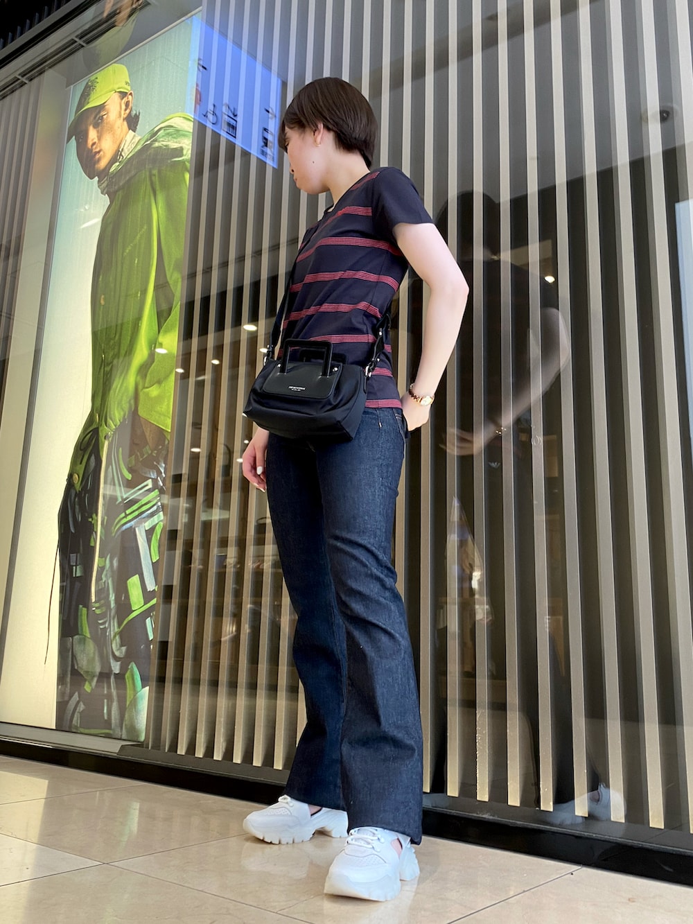 ブラック系のバッグ、ブルー系のデニムパンツ、ホワイト系のスニーカーを着用したレディースの夏コーディネートの3枚目の写真