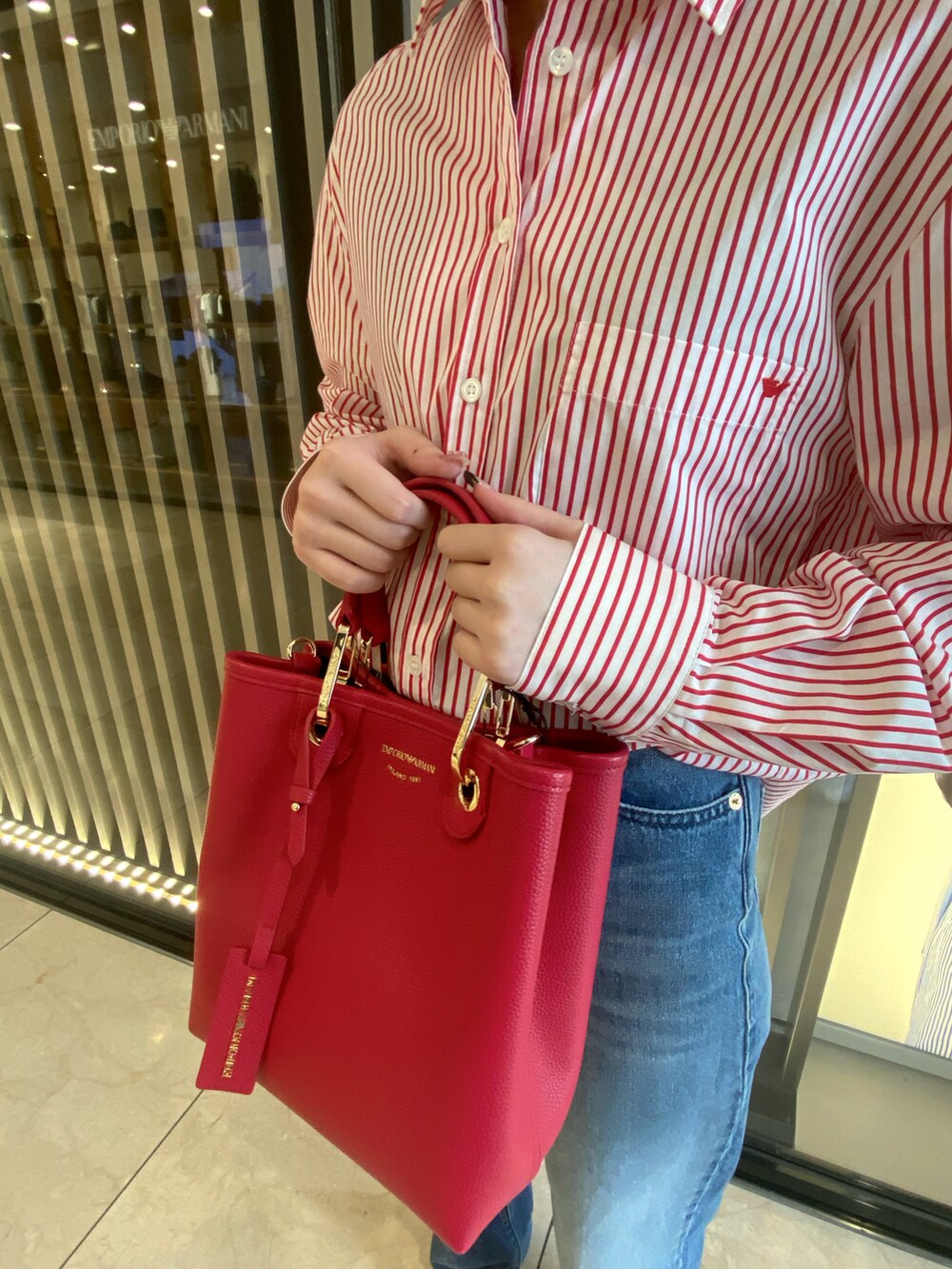 レッド系のシャツ/ブラウス、レッド系のハンドバッグ、ブルー系のデニムパンツを着用したレディースの秋コーディネートの3枚目の写真