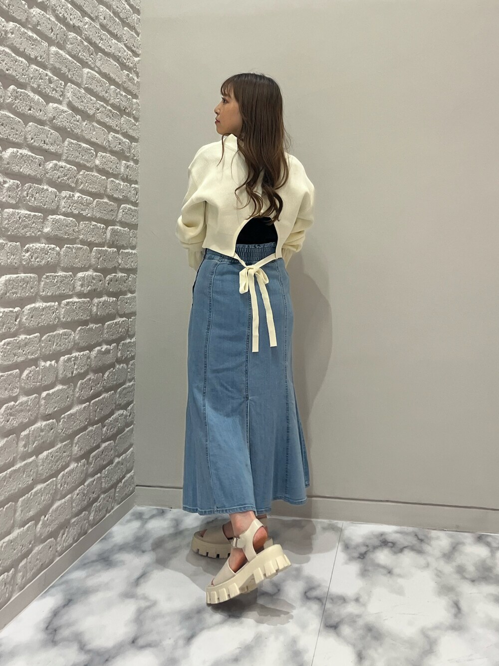 ブルー系のデニムスカート、ホワイト系のカーディガン/ボレロ、ブラック系のTシャツ/カットソーを着用したレディースの春コーディネートの2枚目の写真