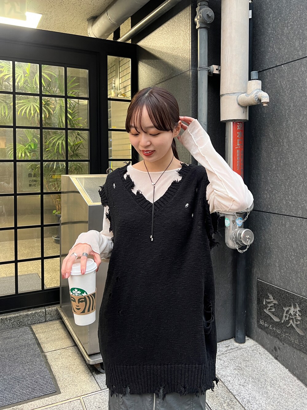 グレー系のスカート、ブラック系のベスト、ブラック系のスニーカーを着用したレディースの冬コーディネートの3枚目の写真