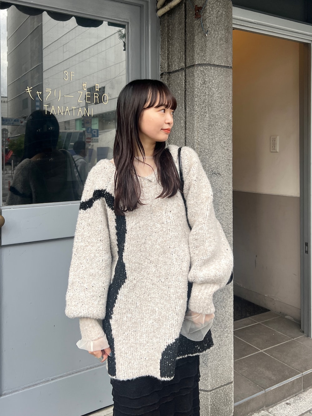 ブラック系のブーツ、ブラック系のスカート、ホワイト系のニット/セーターを着用したレディースの秋コーディネートの2枚目の写真